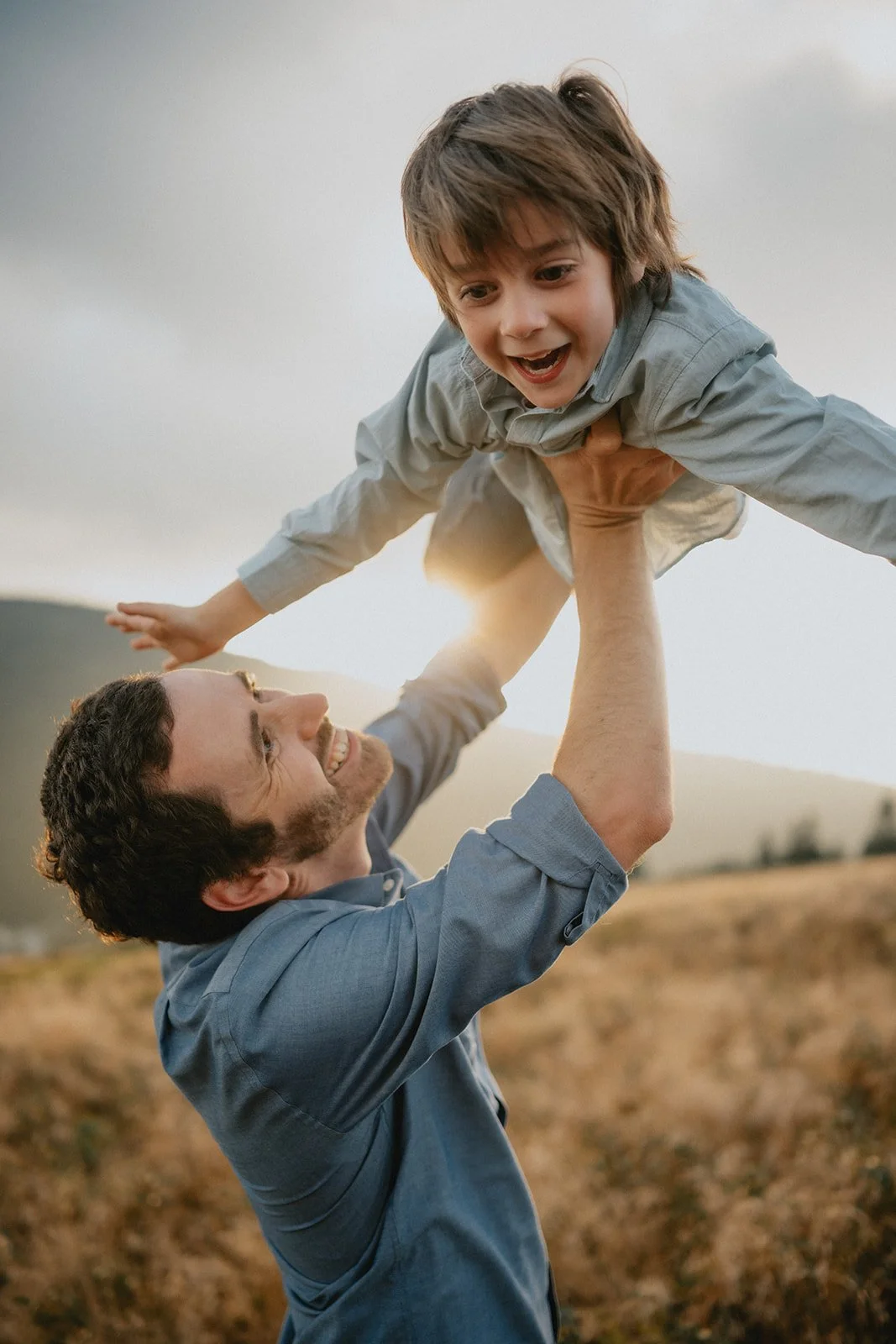 A man lifting a young boy into the air outdoors during sunset, smiling and enjoying the moment.