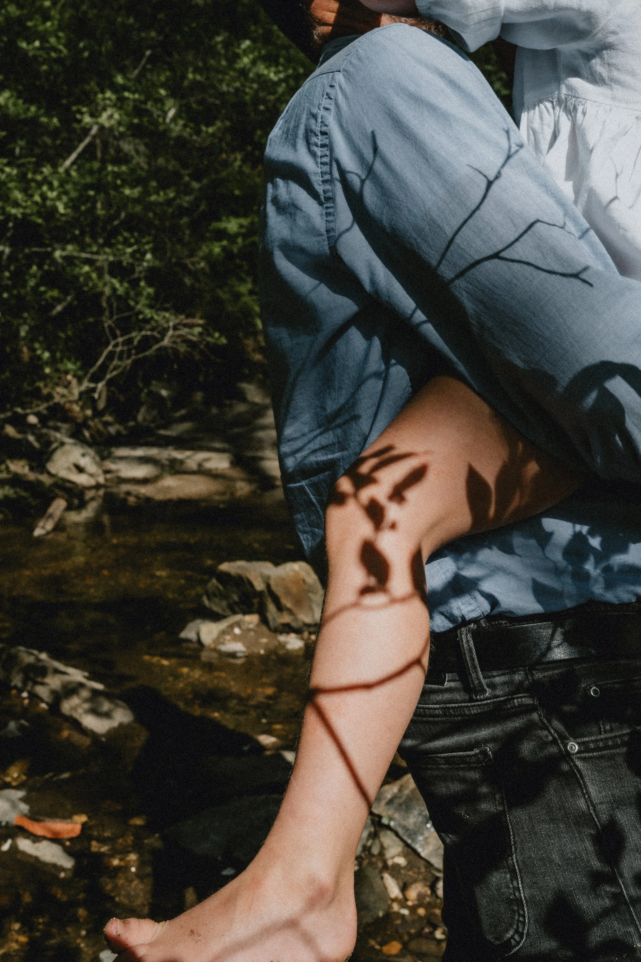 A warm and cinematic moment caught during a family photography session. A pattern of leaves and sticks falls against the leg of a young girl, behind held by her father.