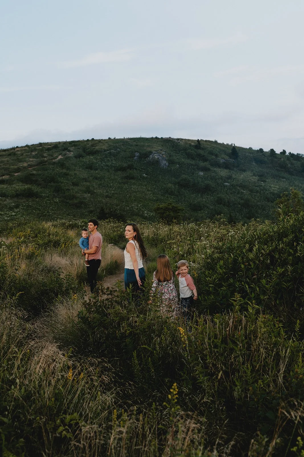 A family of five walking along a grassy trail in a hilly, green landscape.
