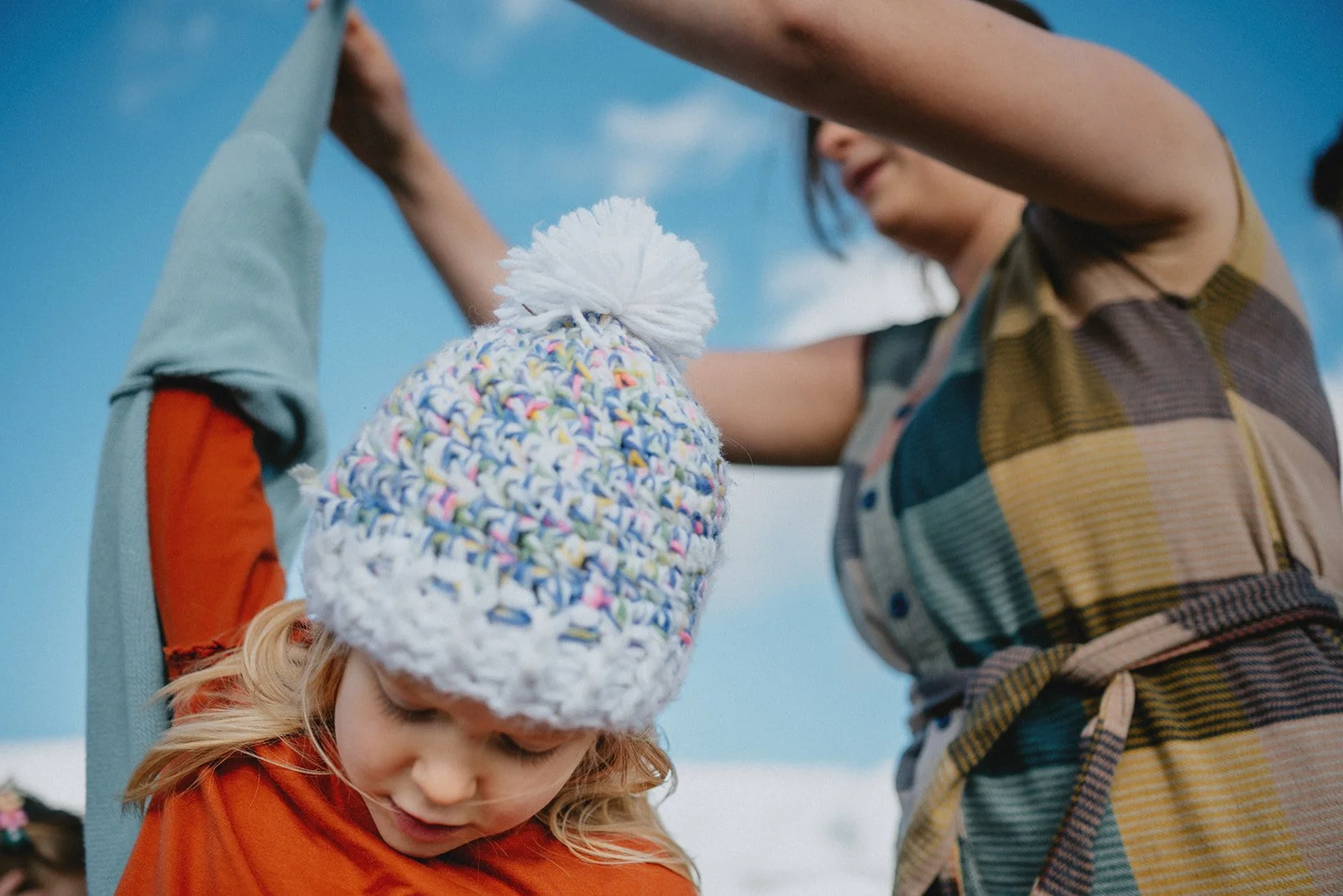 A mom pulls a jacket off of her five year old daughter on a mountaintop with a bright blue sky behind them on Black Balsam Knob outside of Asheville.