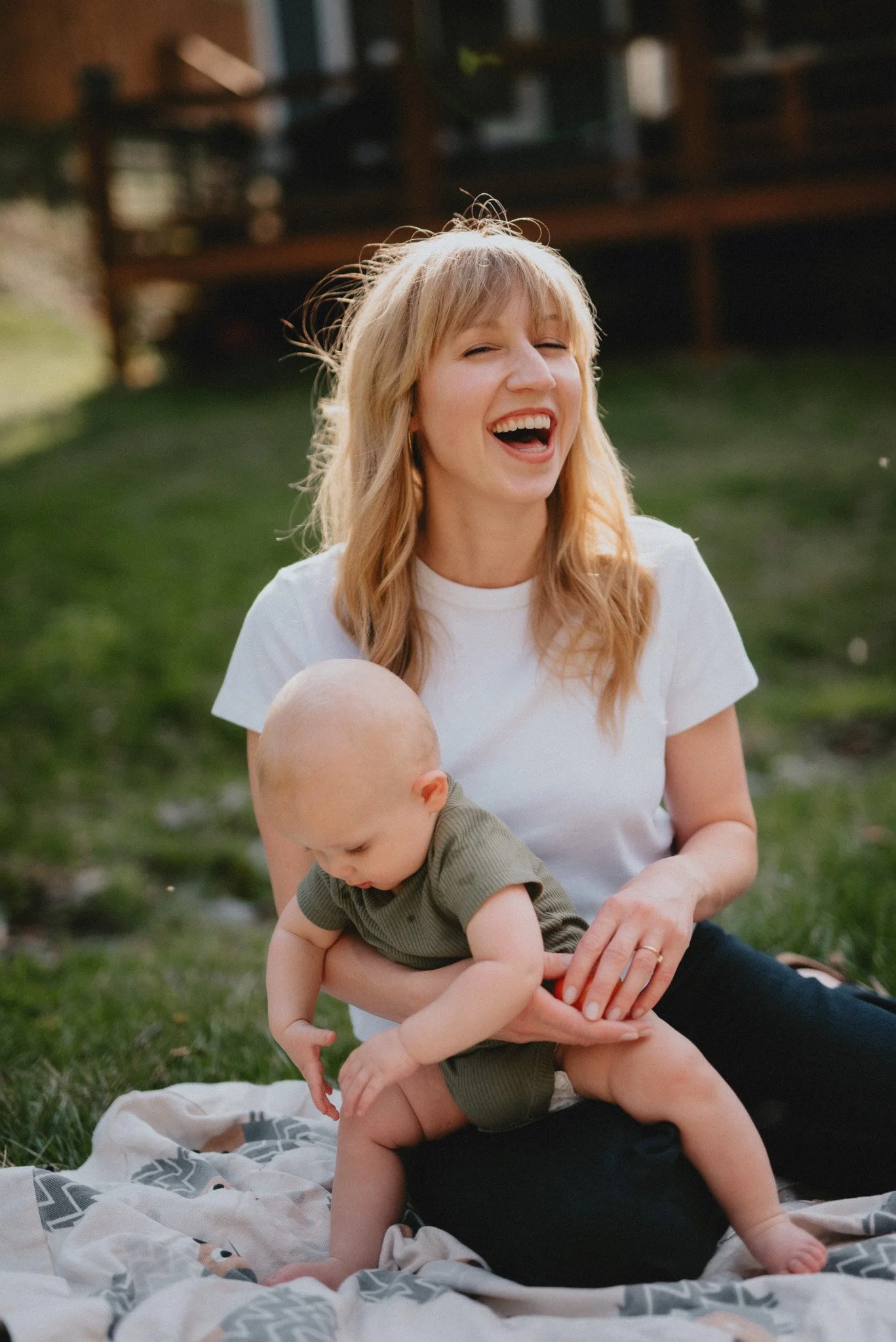 a beautiful mother sits outside on a blanket holding a baby on a spring day in Asheville, North Carolina, posing for a family photograph.