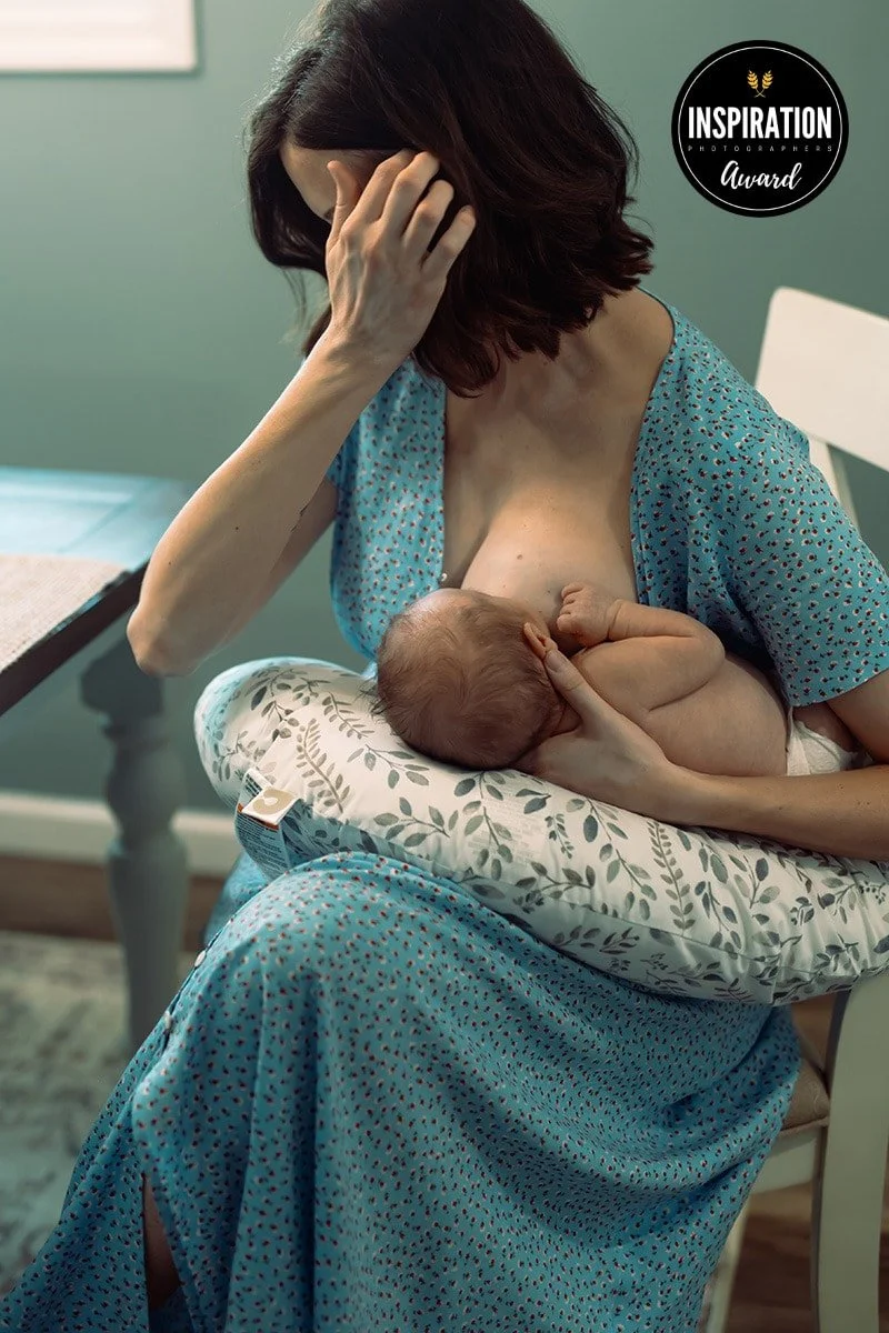 A woman in a blue dress breastfeeding a newborn baby while sitting on a chair in a room with green walls.