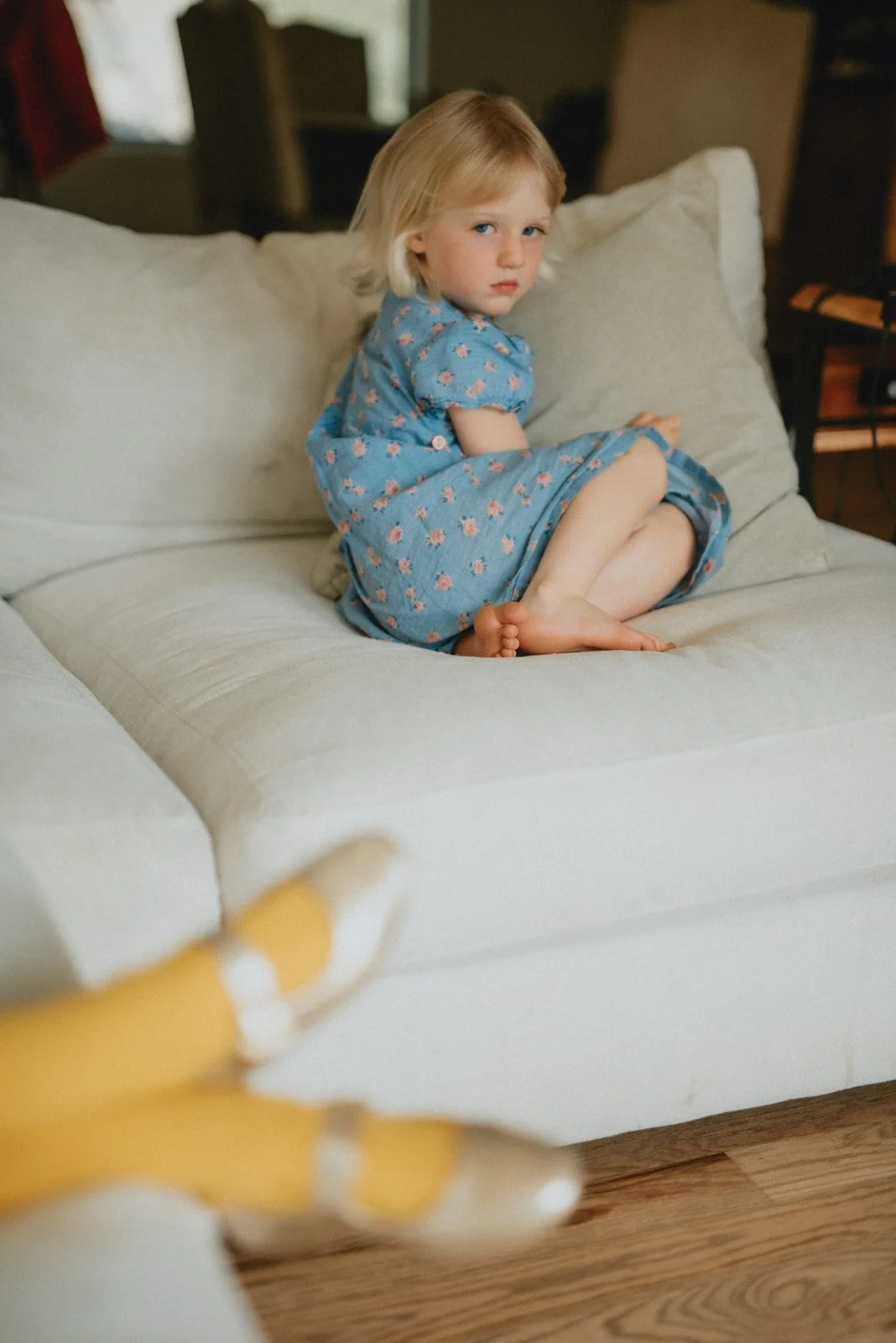 a young girl in a blue dress looks at the camera without a smile. There are golden shoes in the foreground.