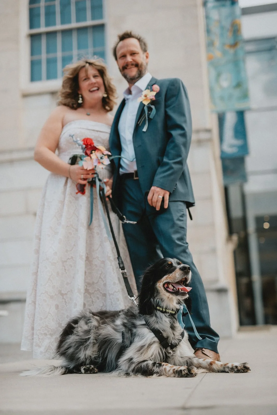 a couple and their dog smile for a wedding picture outside the art museum in downtown asheville, North Carolina