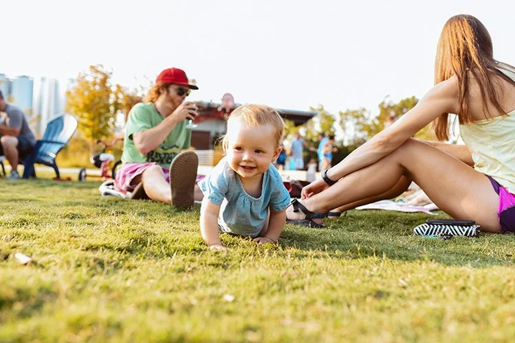 A baby crawls with a big smile through the bright yellow green grass of New Belgium Brewery in West Asheville, North Carolina