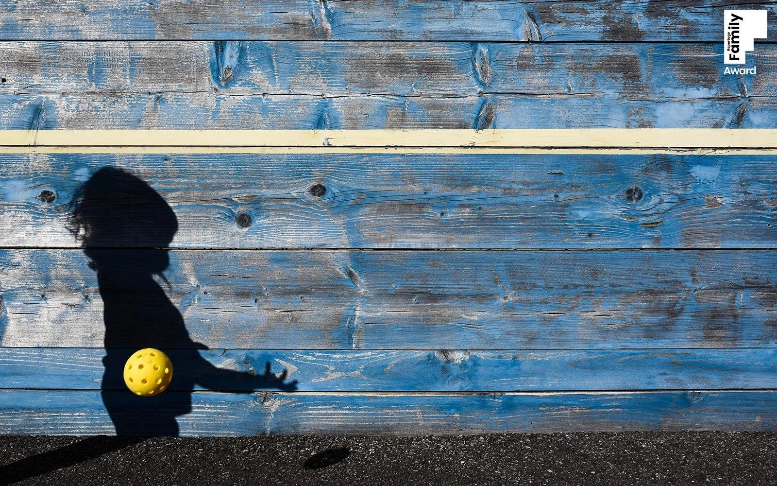 Shadow of a child playing with a yellow ball on a wooden blue wall background.