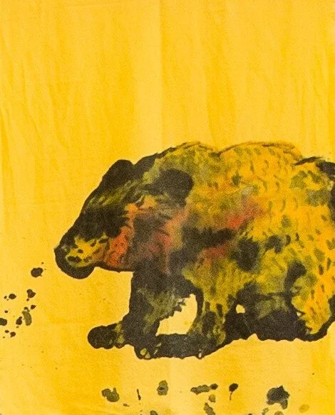 A drawing in paint on fabric of a brown bear outline with a few orange bits of colour. The bear is towards the bottom right of the image. 