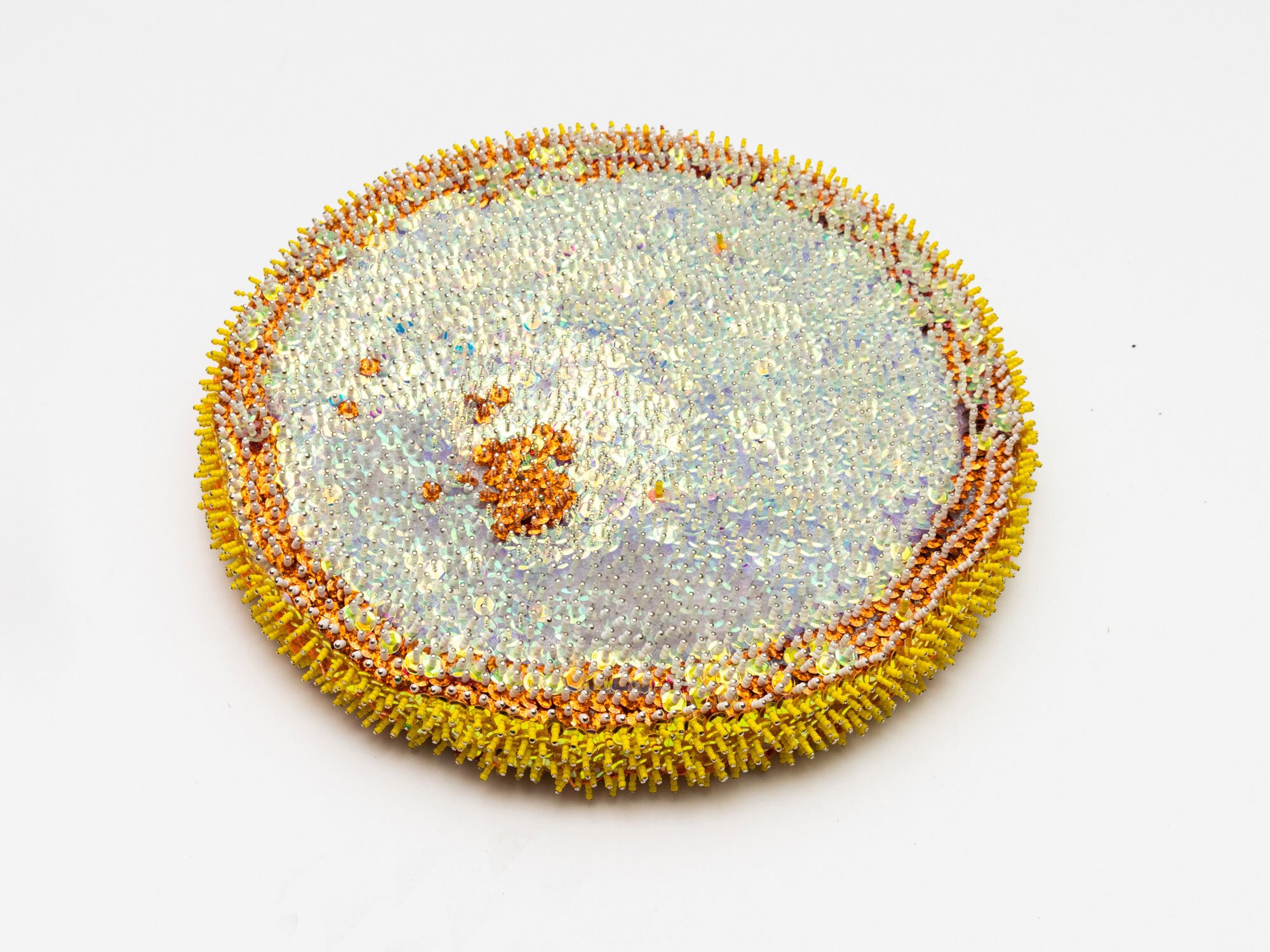 The other side of a flat 3D circular piece with pins in white, pale grey, orange and yellow. 