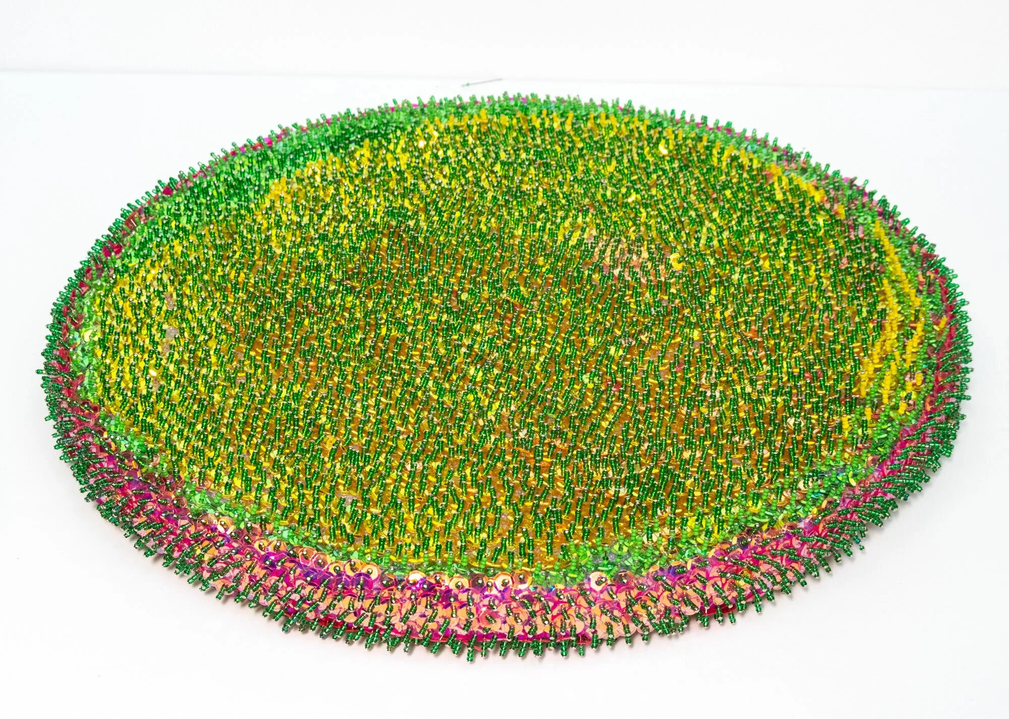 One side of a flat circular piece covered in pins in shades of green, yello and pink around the edge.