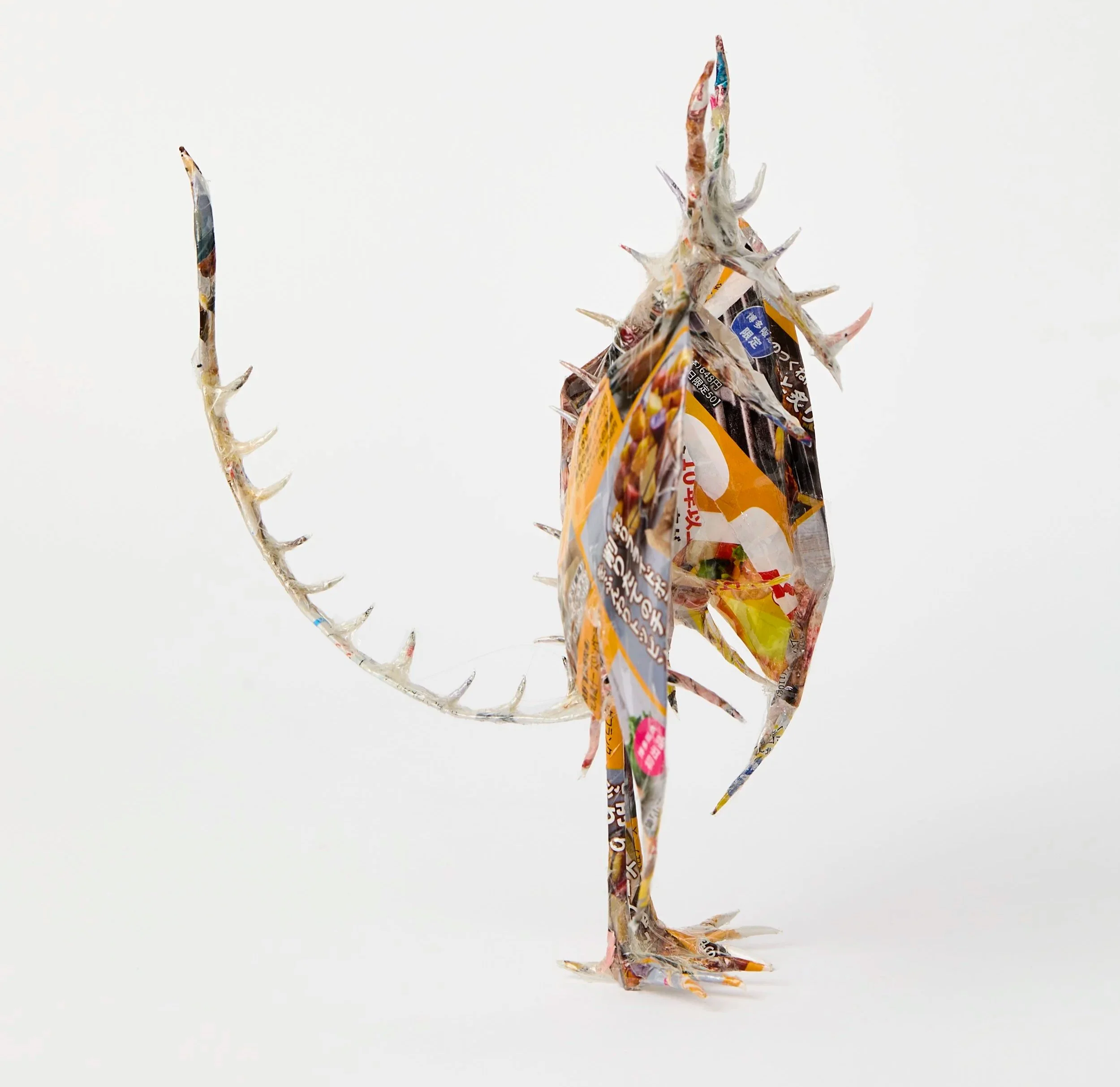 Dragon with 2 large wings, standing on 2 legs with 2 arms hanging down & claw-like hands. Spikes on ridge down back & on tail. The head has 2 horns, spikes & a beak-like open mouth