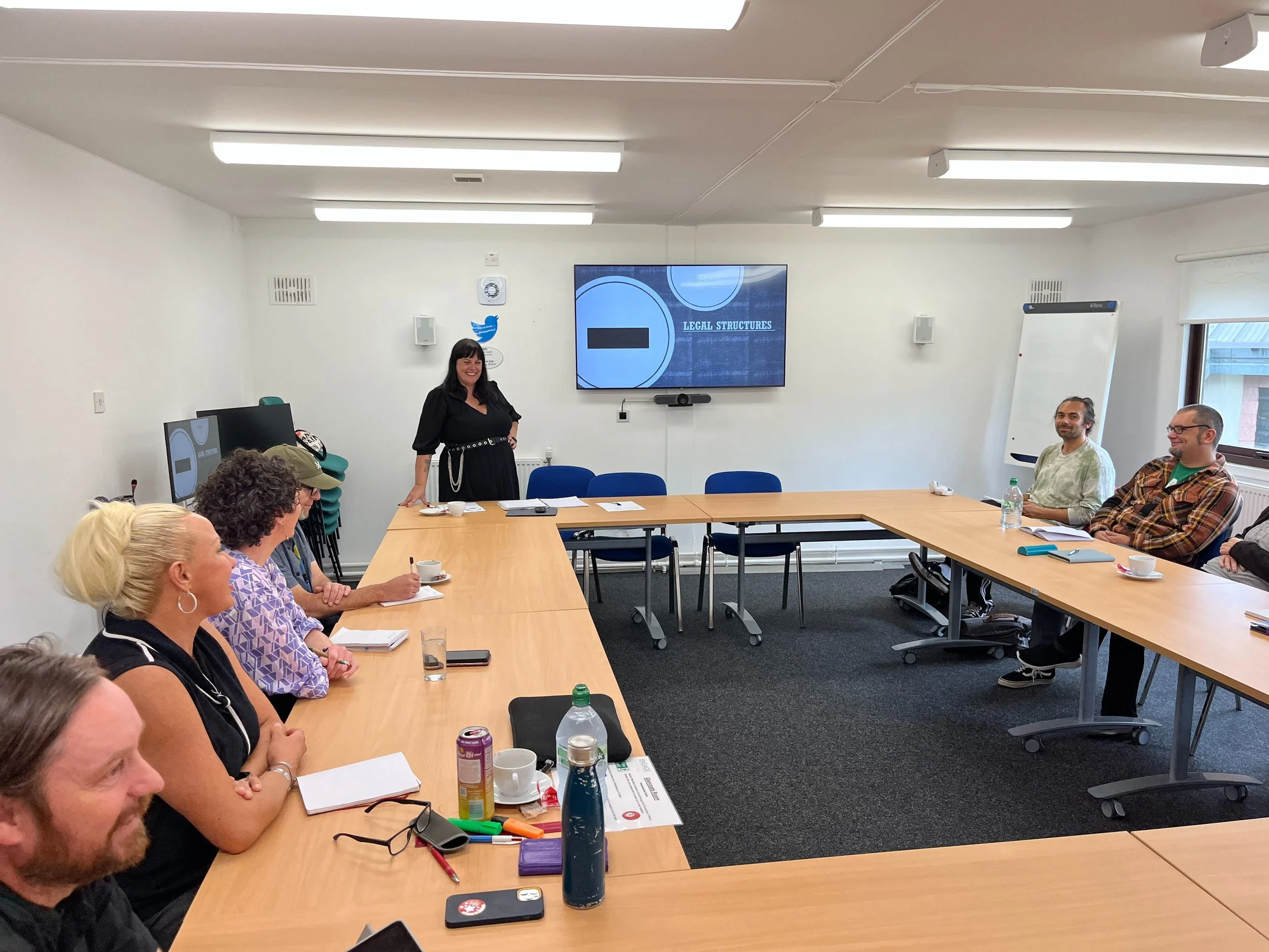 A woman giving a presentation to a group in a conference room with a screen displaying 'Legal Structures'.