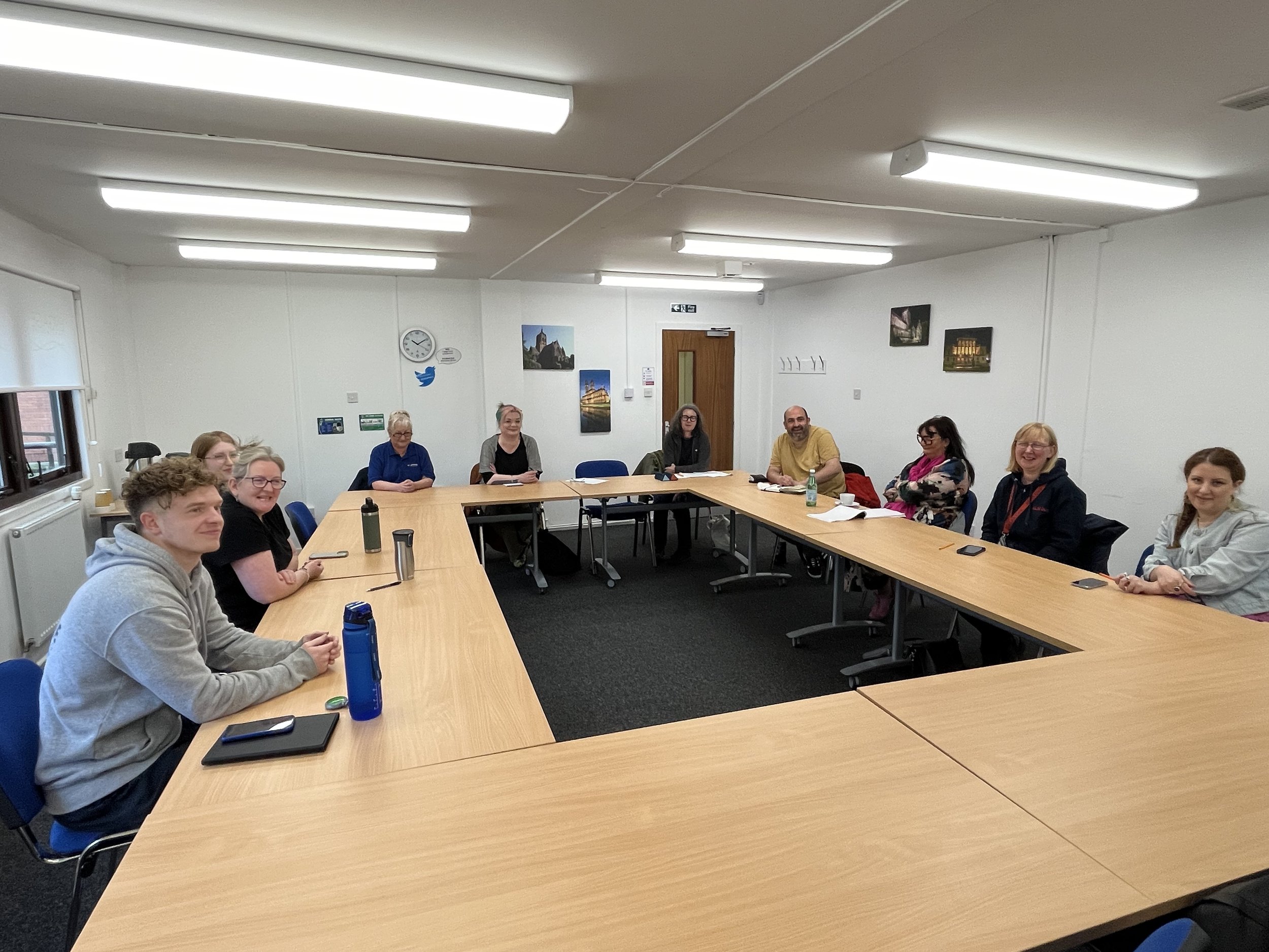 A group of people sitting around a rectangular conference table in a meeting room, smiling and looking at the camera.