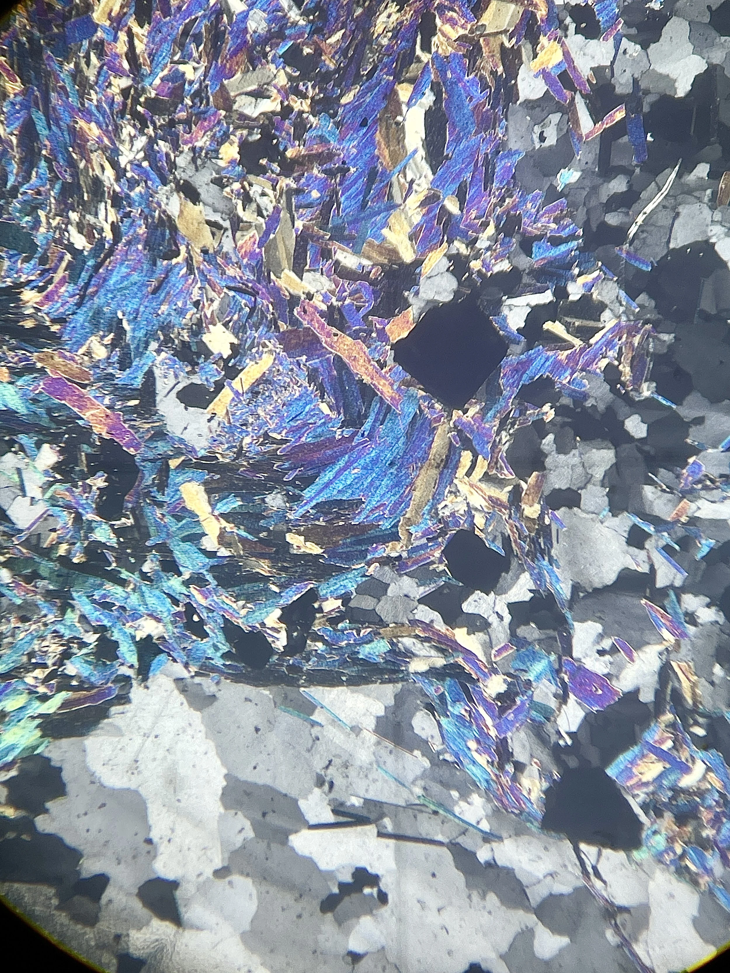 Close-up view of a mineral or crystal formation with iridescent, metallic, and multicolored shards on a rough surface.