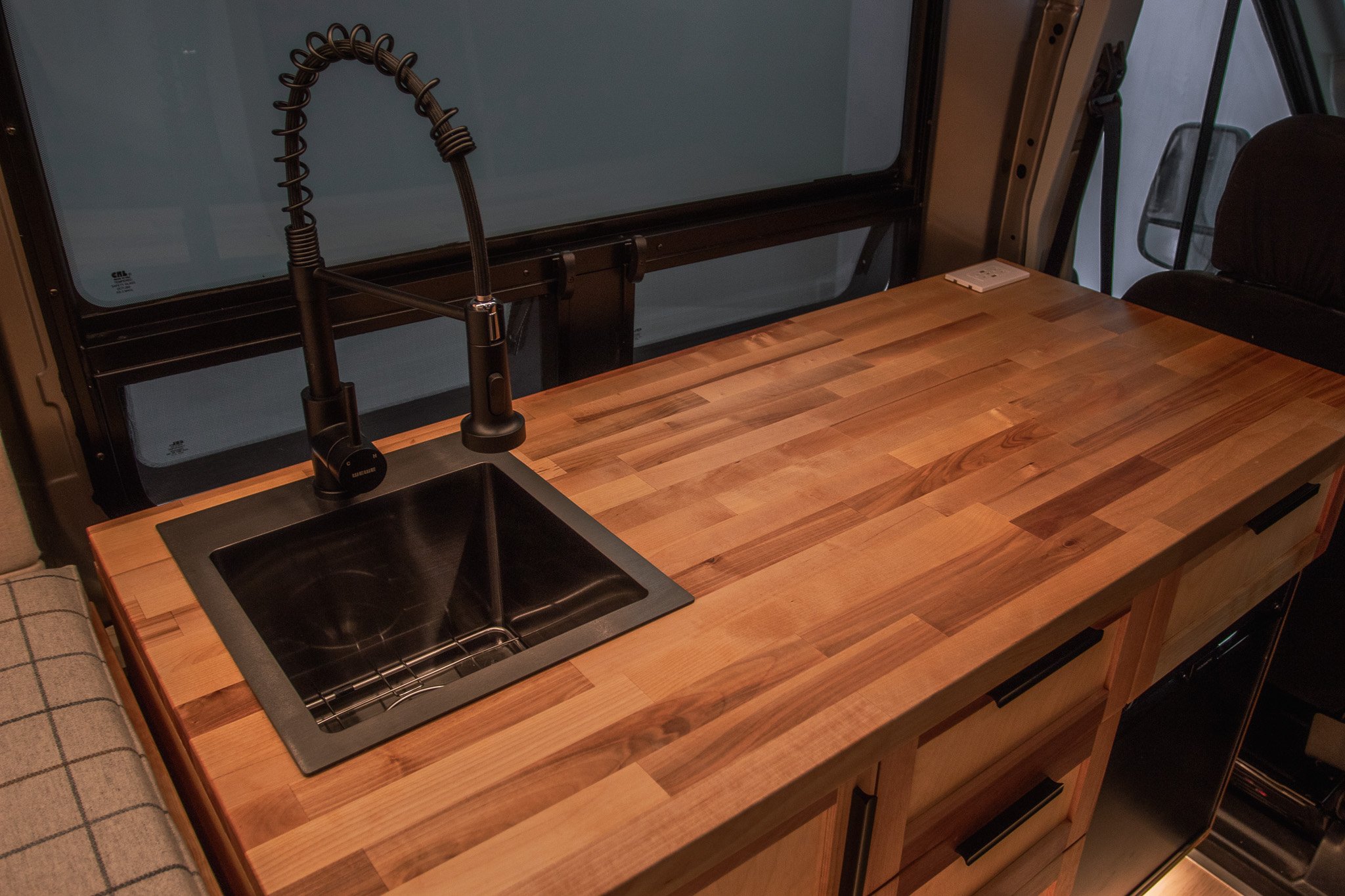 Camper van kitchen with wooden countertop, black faucet, and sink.