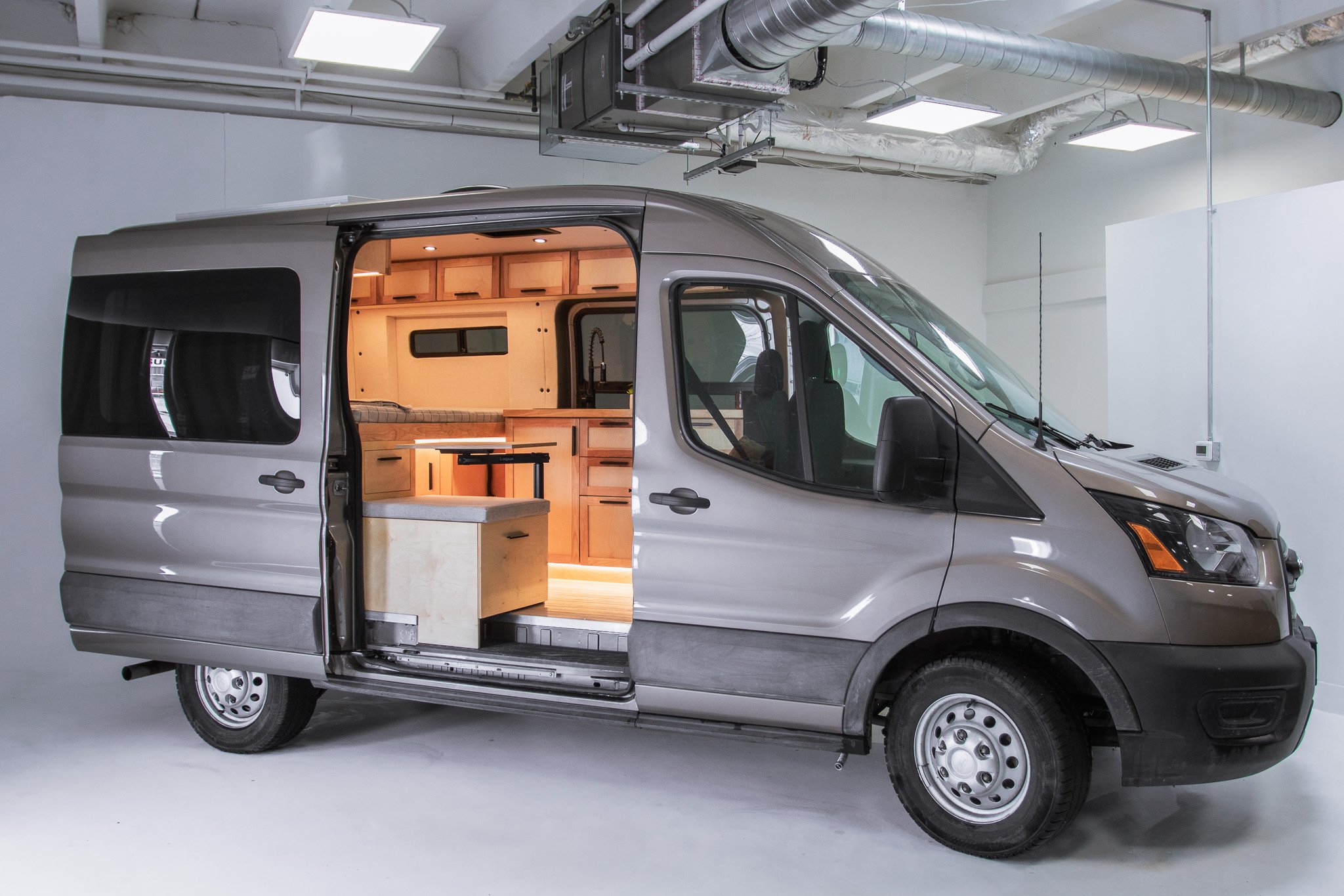 Camper van with open sliding door showing interior cabinetry and couch inside a garage.