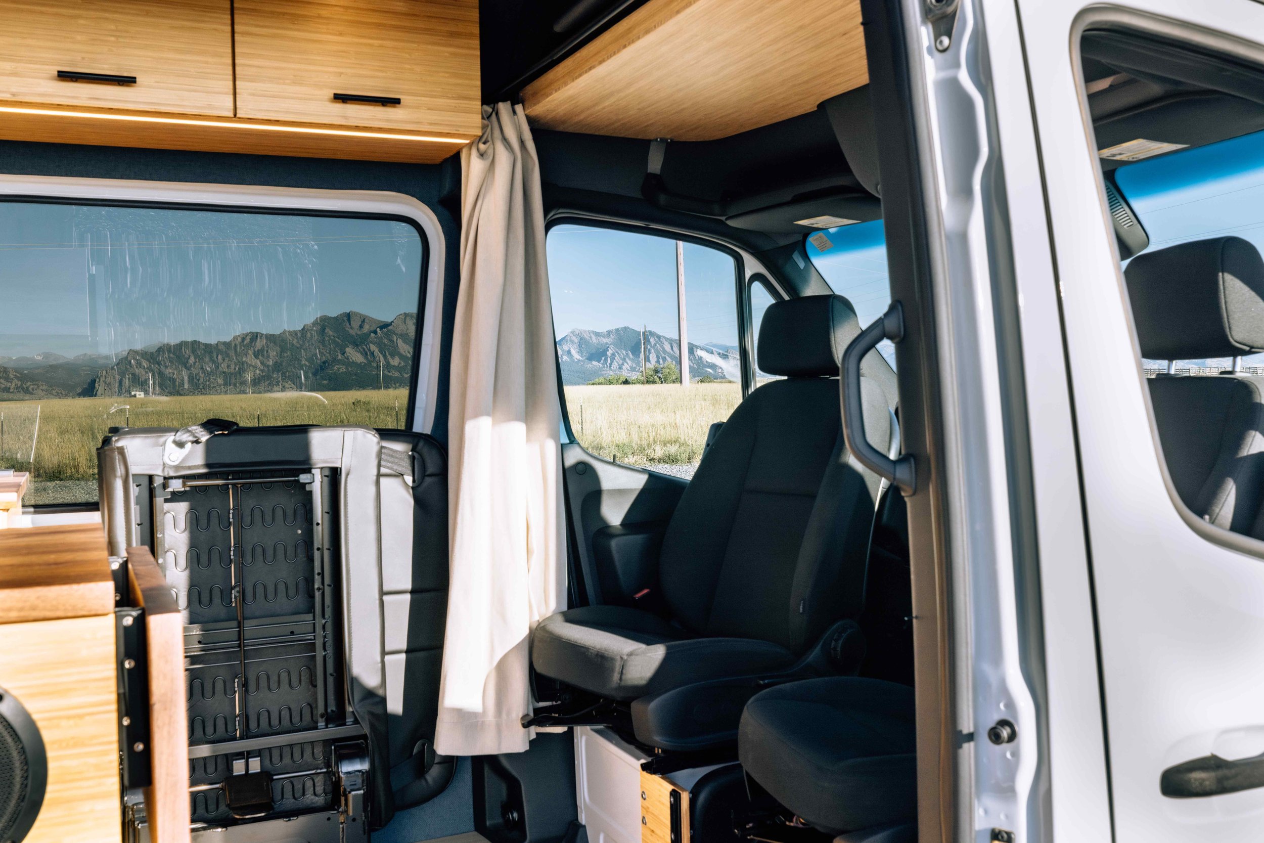 Van interior with seating and cabinets, mountain view through window.