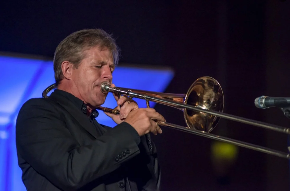 Executive Director Scott Garlock playing a trombone on stage with a dark background