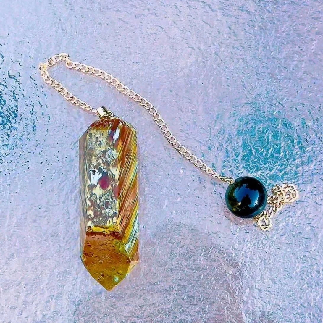 Material: Amphibole Quartz & Sheen Obsidian 
Pendulum  
Sold  
This pendulum is made out of a high-quality piece of Amphibole Quartz with gold-colored hardware and a large Sheen Obsidian end bead.
