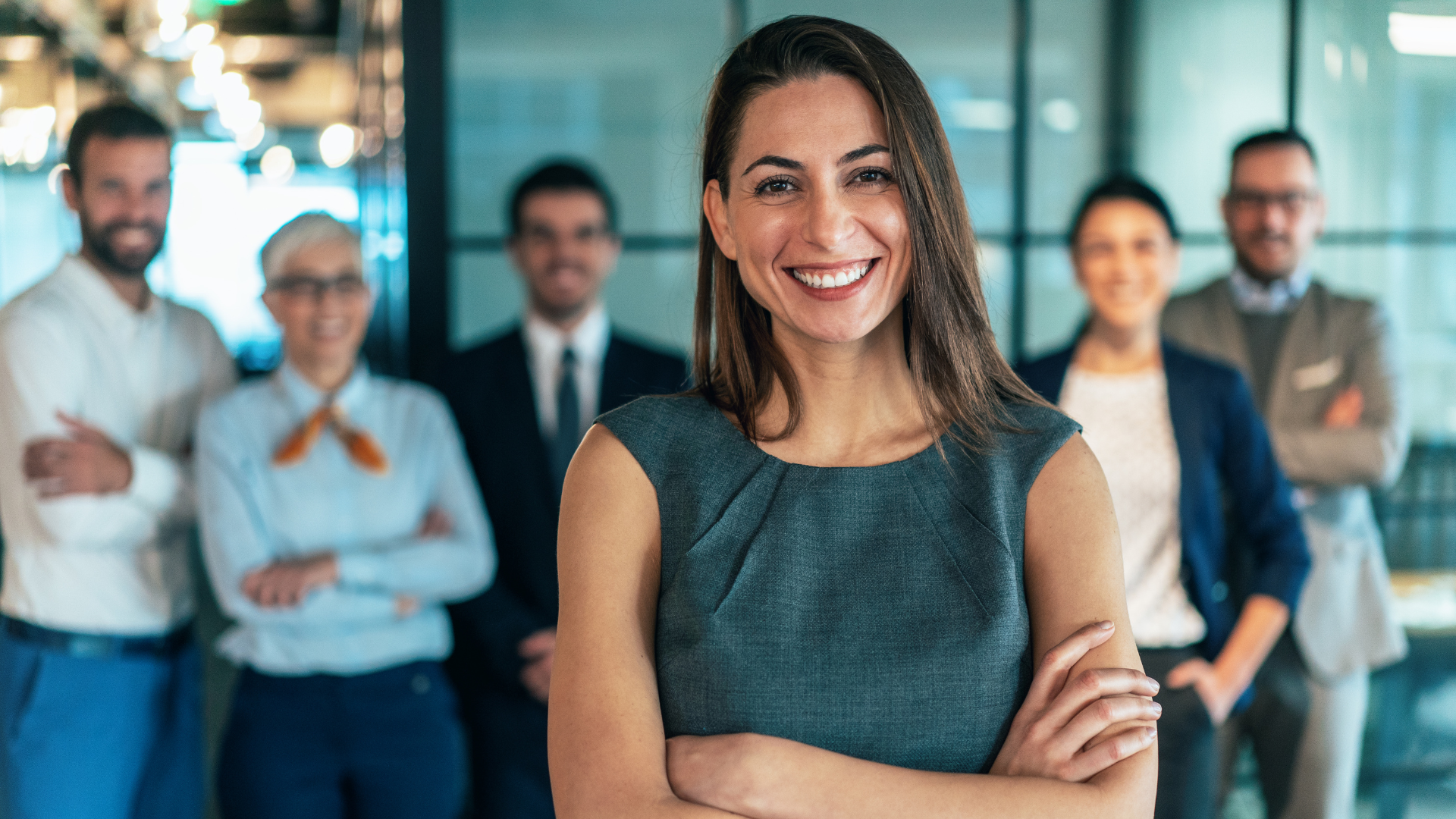 Confident woman standing with her arms crossed looking at the camera with her team behind her