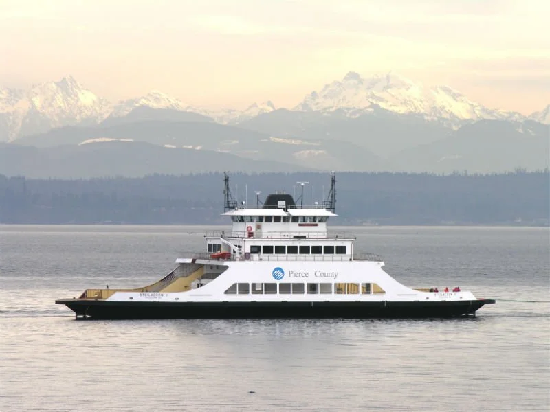 Ferry boat on a body of water with snow-capped mountains in the background.