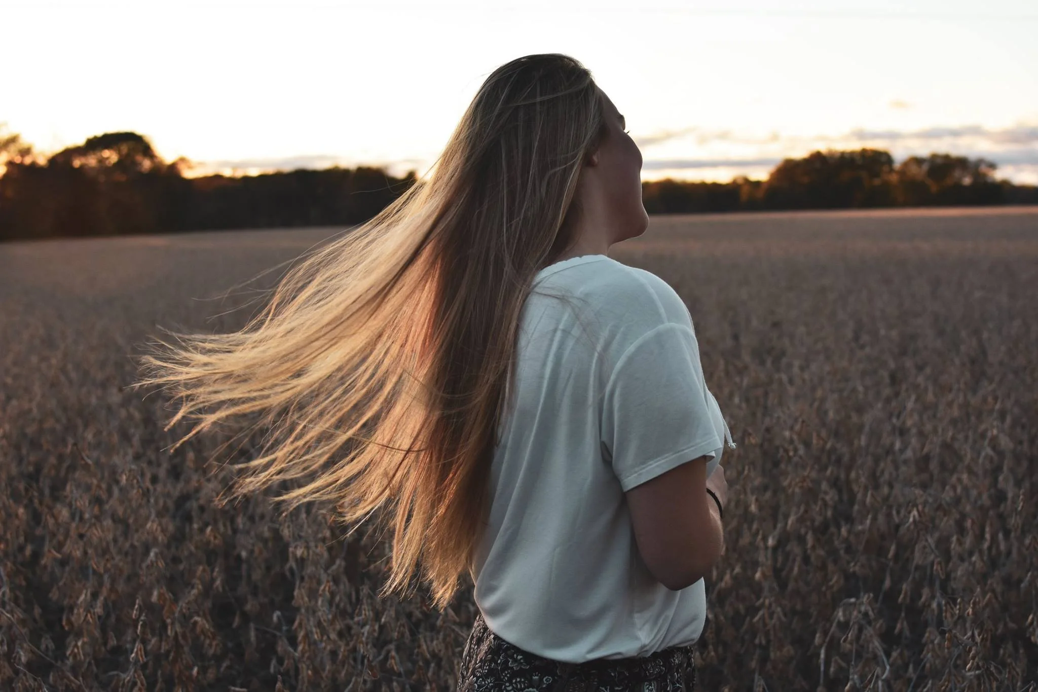 Woman with long hair standing in a field at sunset