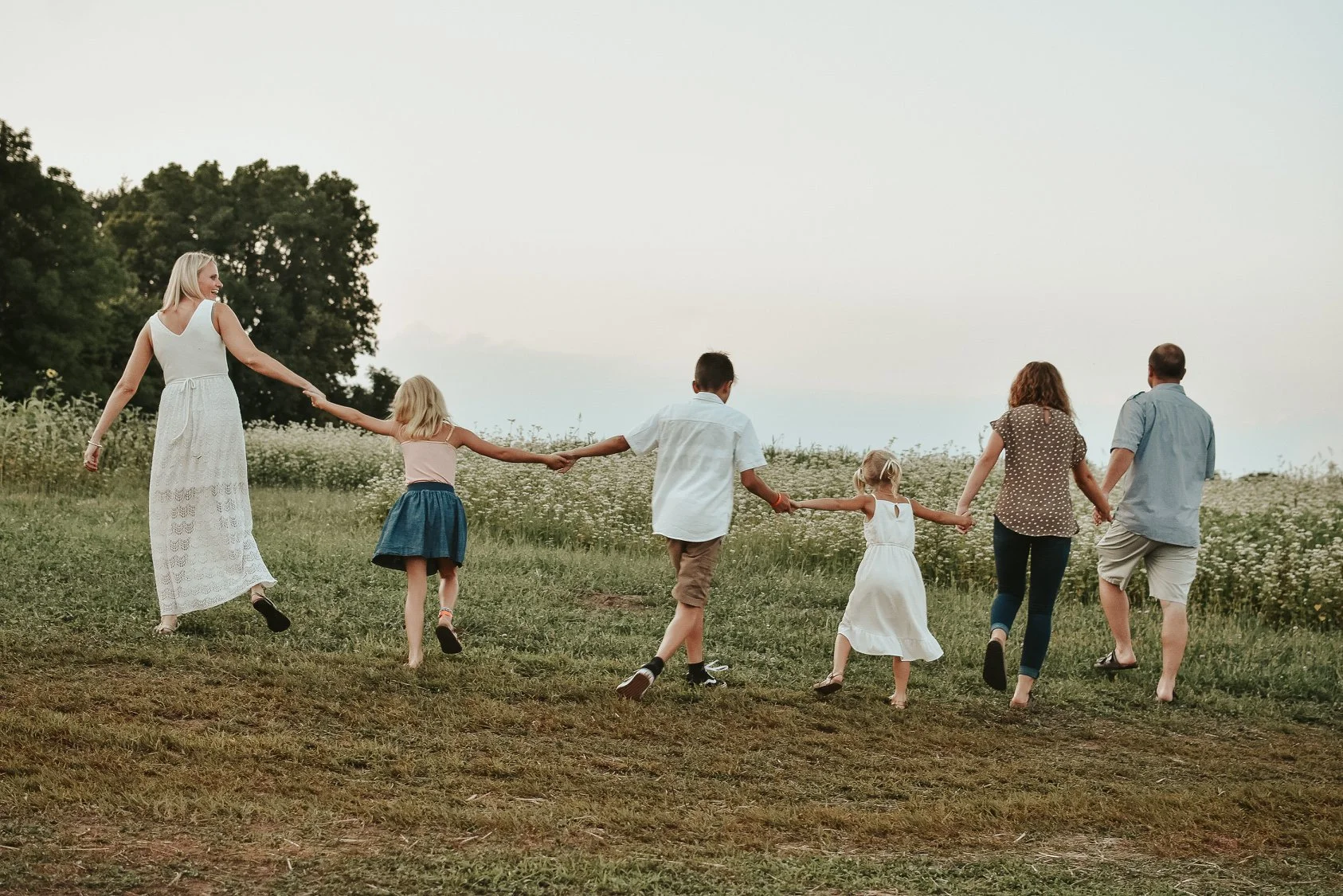 Family walking hand-in-hand in a grassy field under a clear sky.
