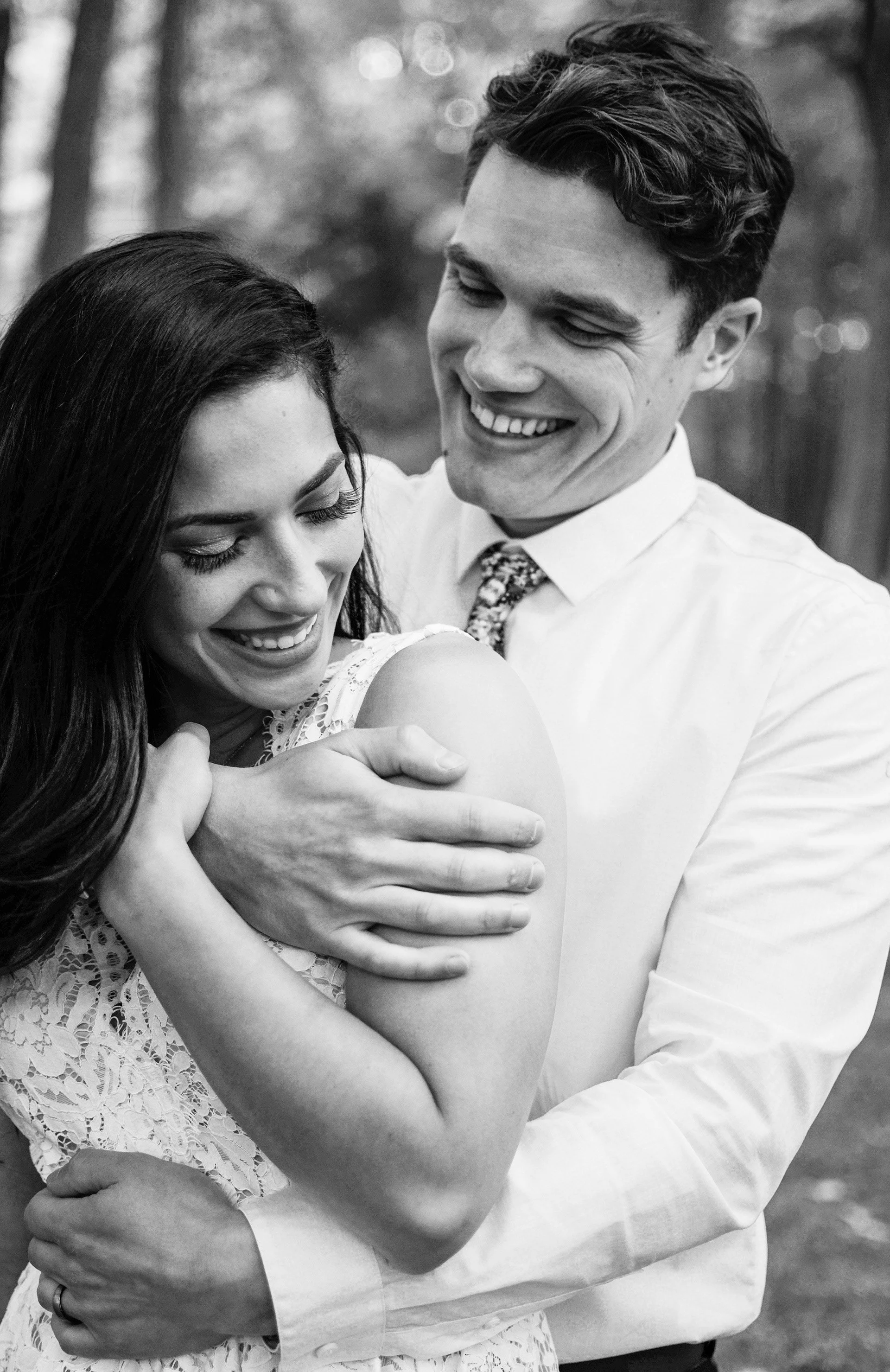 Black and white photo of a couple embracing, both smiling, in an outdoor setting.