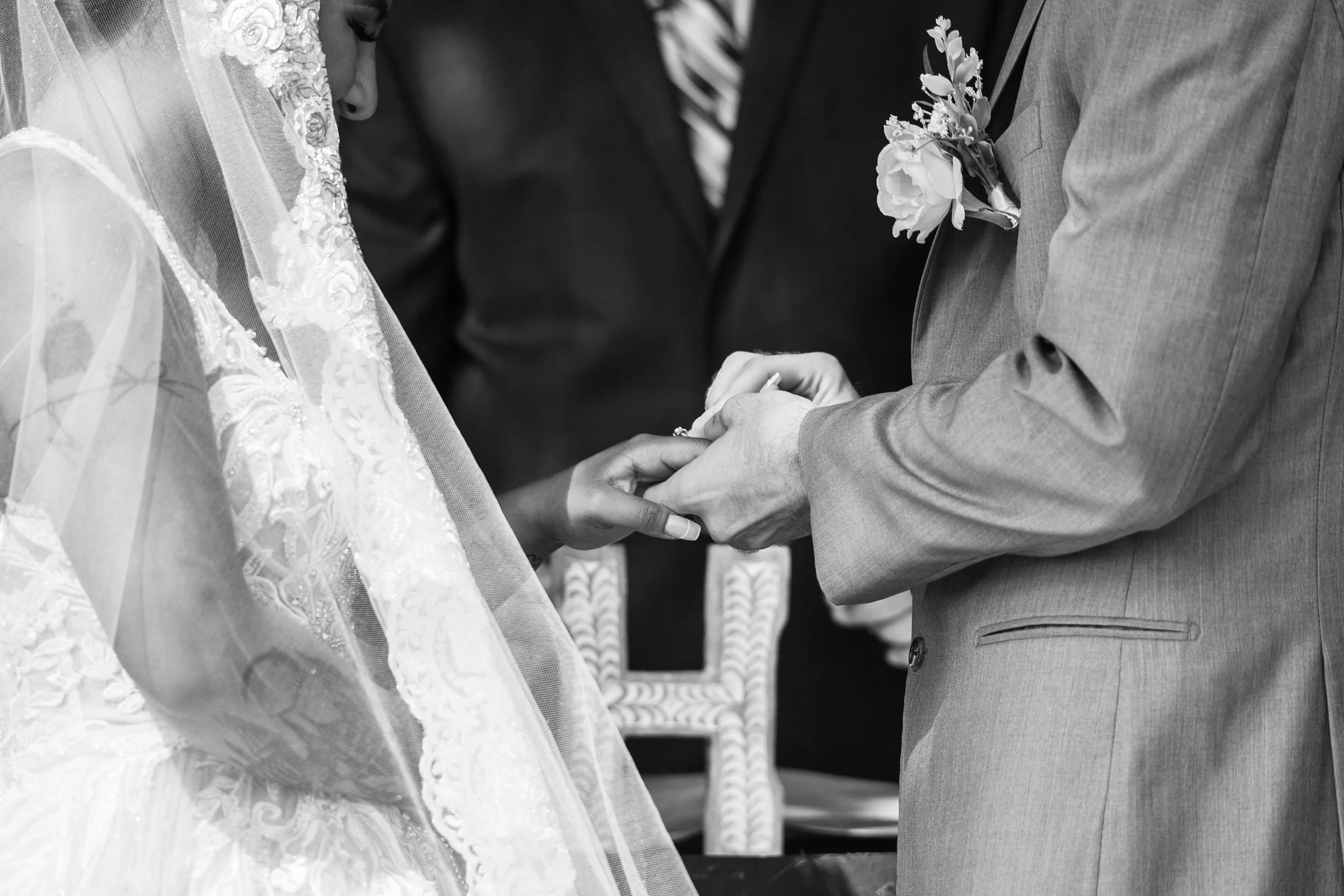 Black and white photo of a wedding ceremony with a bride in a veil and groom in a suit exchanging rings.