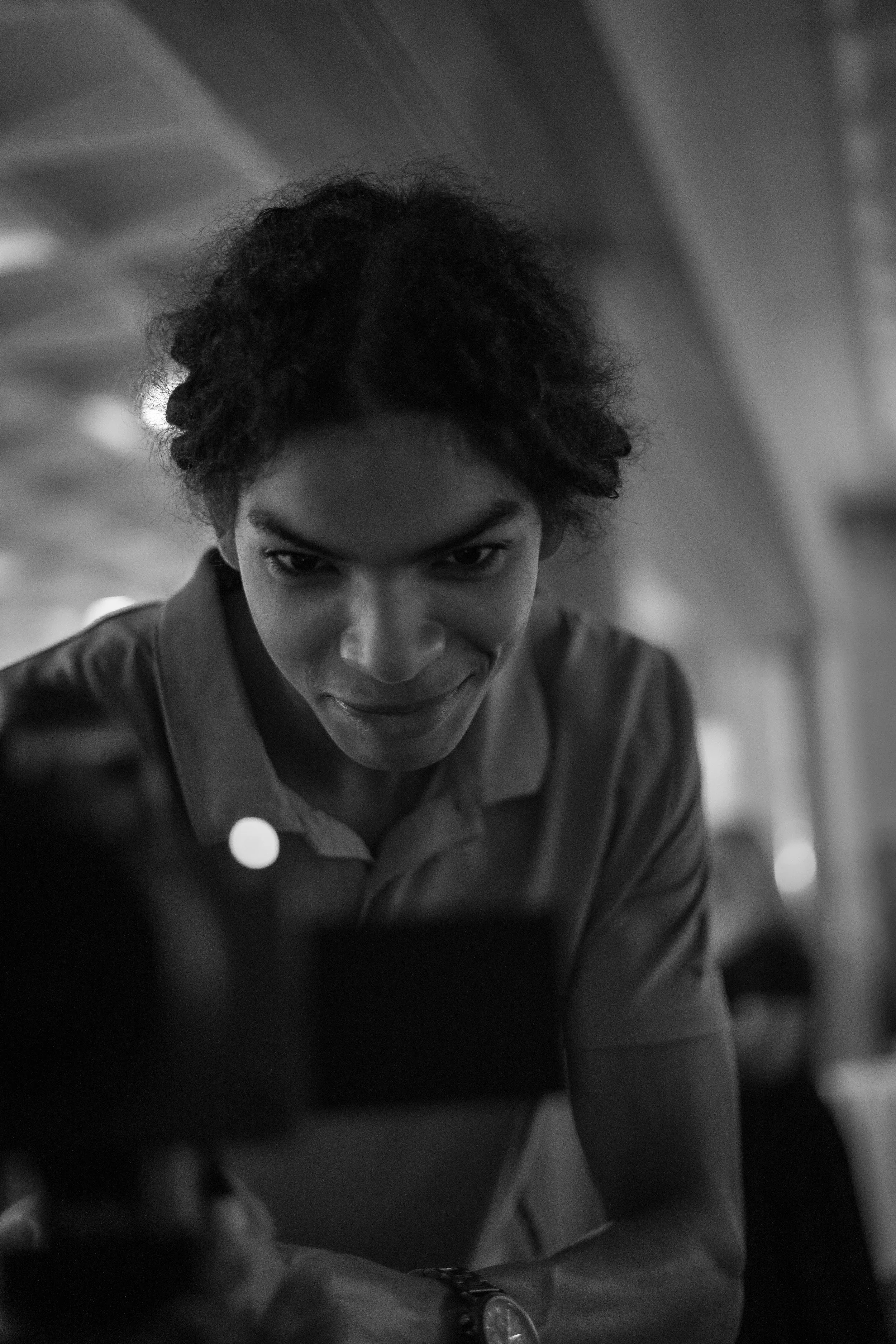 A person with curly hair looking at a camera screen in a grayscale photo, indoors.