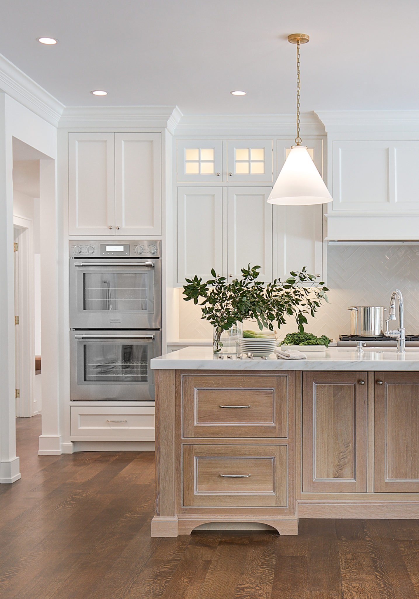 Kitchen with white cabinets, wooden island, double ovens, pendant light, and greenery.