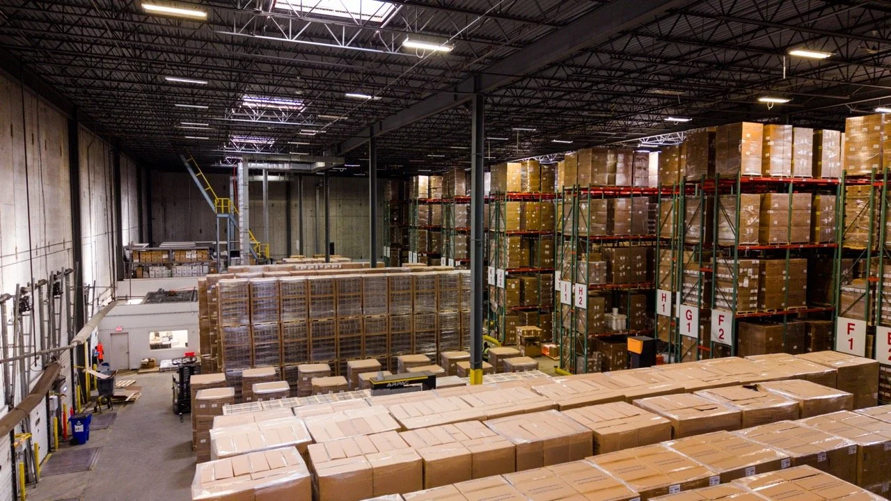 Wide interior drone photo of the warehouse at 655 Church St in Bayport, NY, showing the full depth of the space, the high ceiling, pallet racking, and rows of staged pallets.
