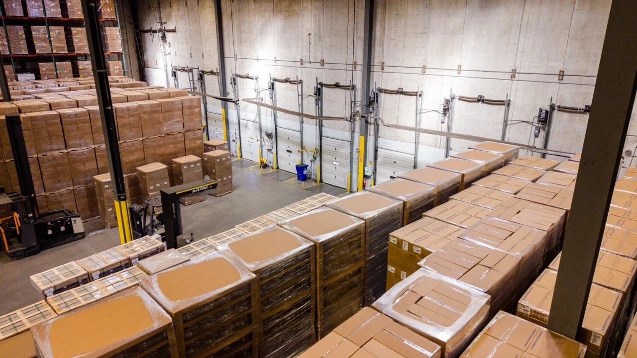 Interior drone photo of the loading dock wall at 655 Church St in Bayport, NY, with a row of dock doors, a forklift, and rows of wrapped pallets staged on the warehouse floor.