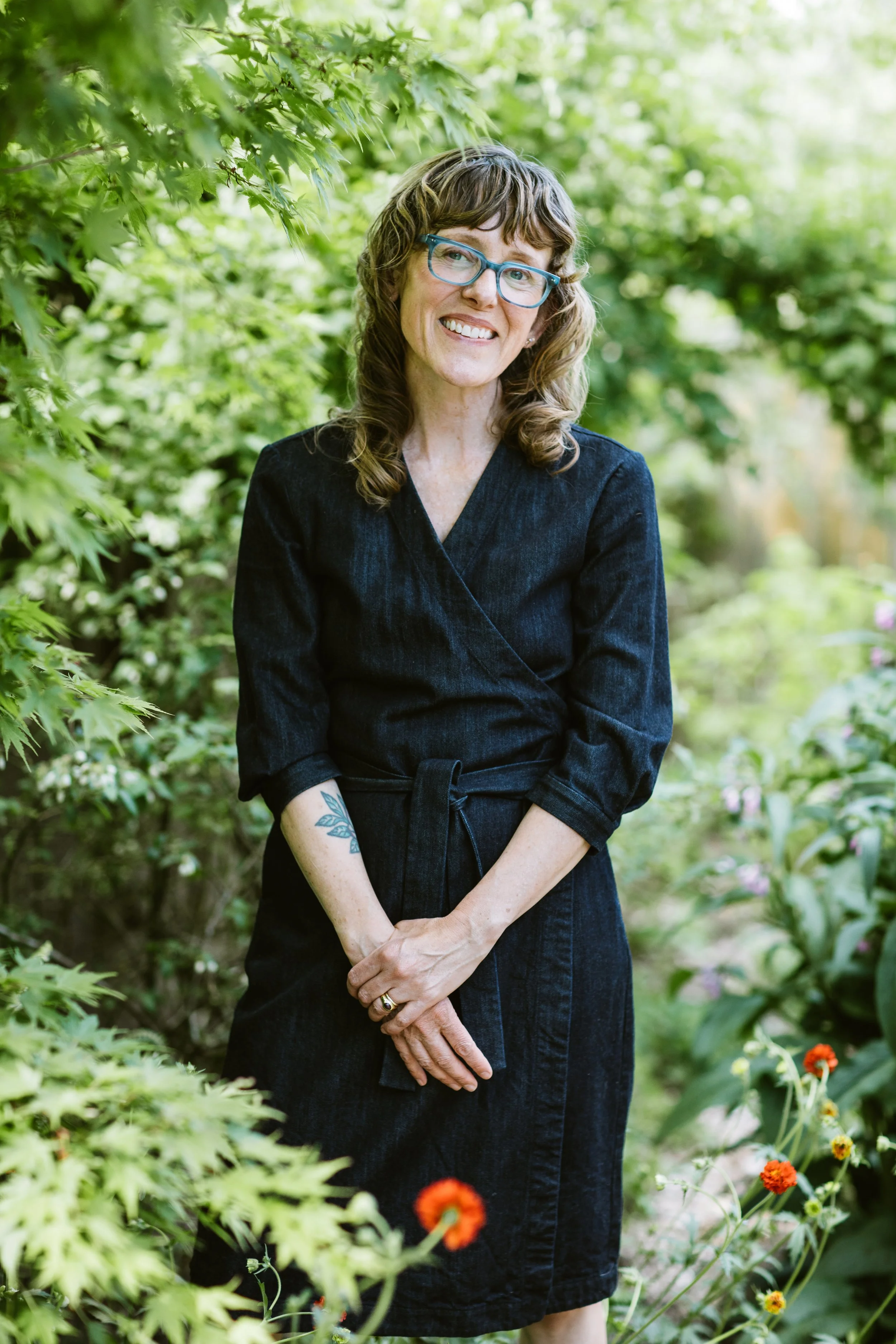 Photograph of a female identifying life coach in middle age, standing in her garden and smiling warmly.