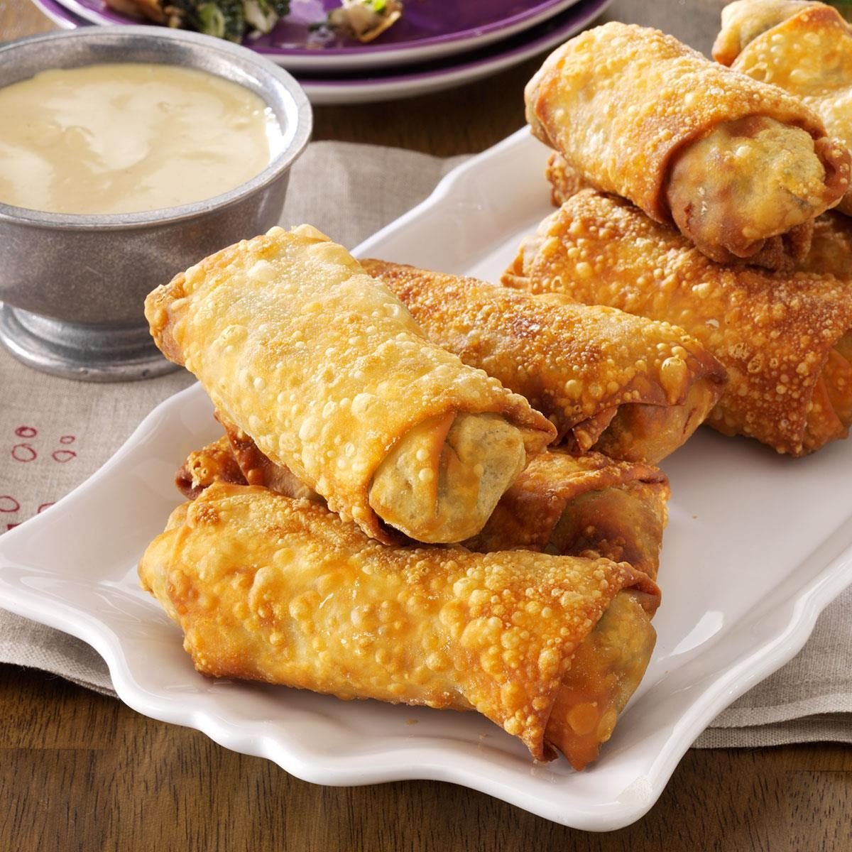 Fried eggrolls on a white platter with dipping sauce and salad in the background.