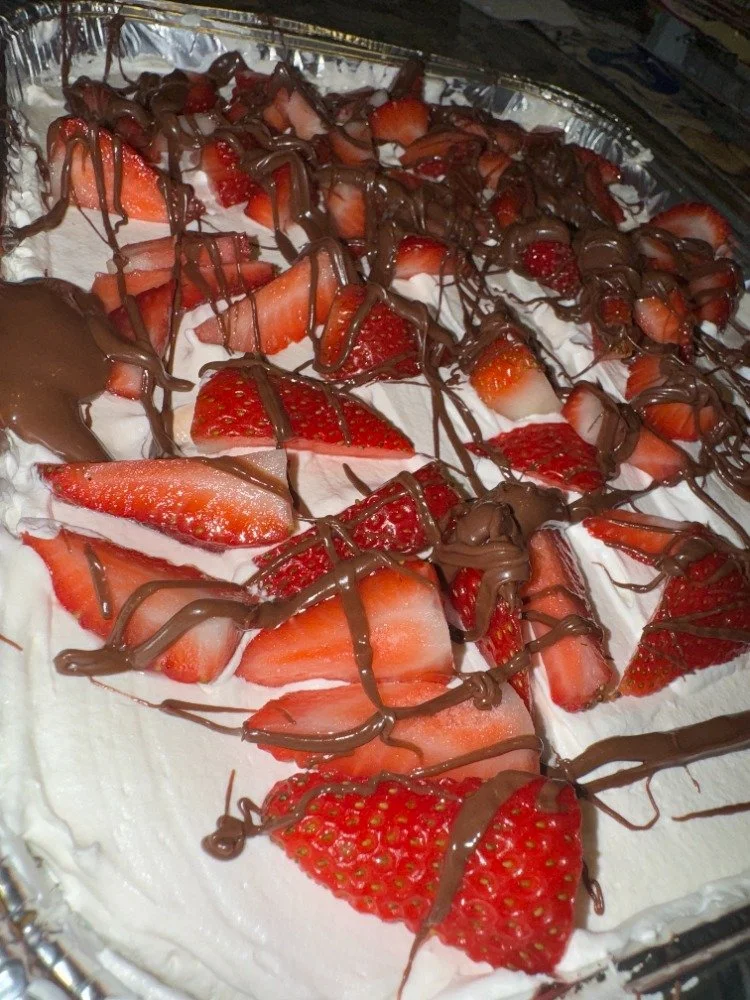  Strawberry tres leche cake dessert with sliced strawberries, whipped cream, and drizzled nutella.