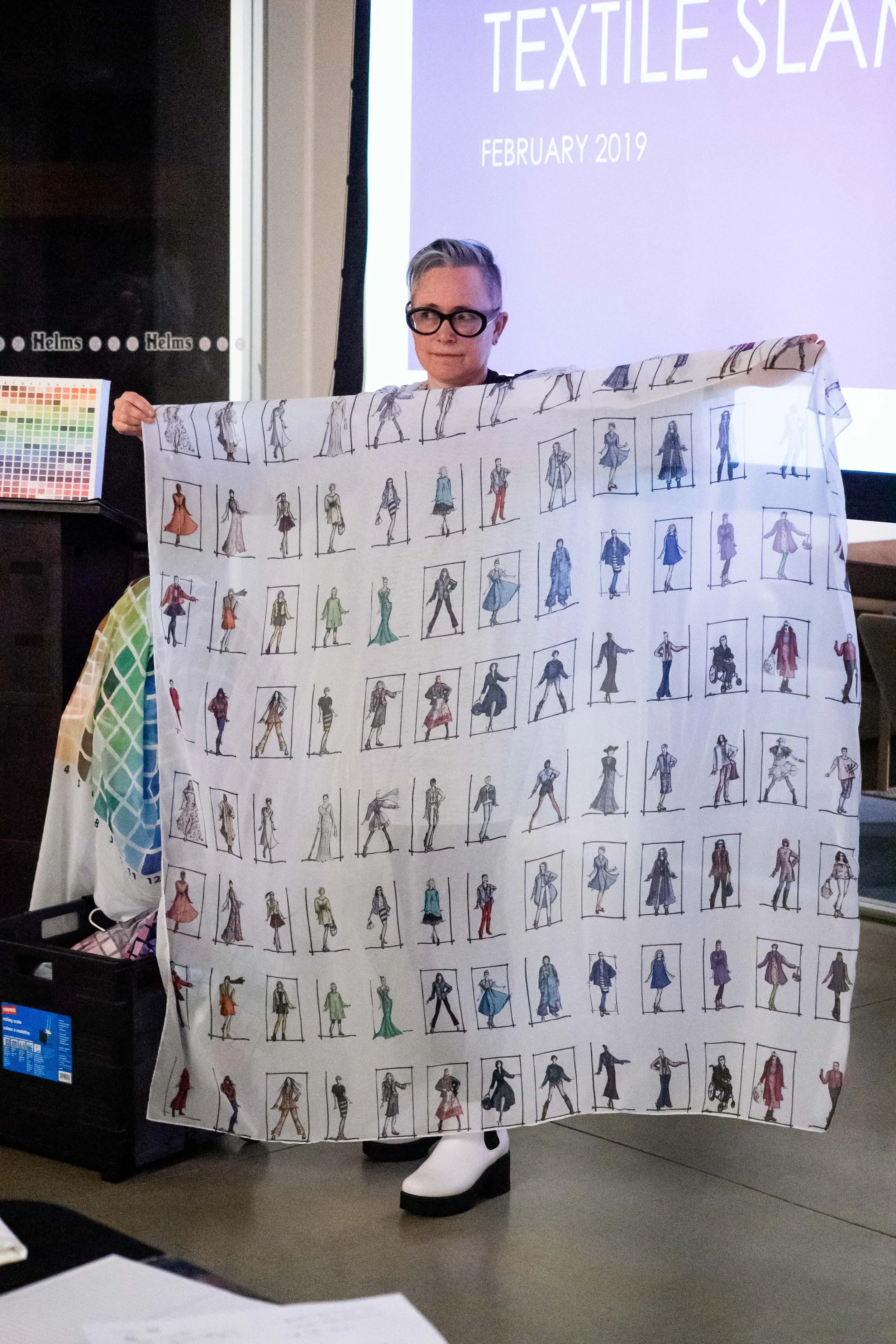 Person holding a fabric with multiple fashion sketches