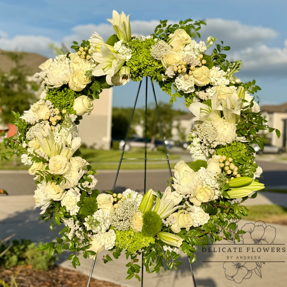 Elegant white and green standing sympathy wreath featuring lilies, roses, hydrangea, and seasonal greenery by Delicate Flowers by Andreea.