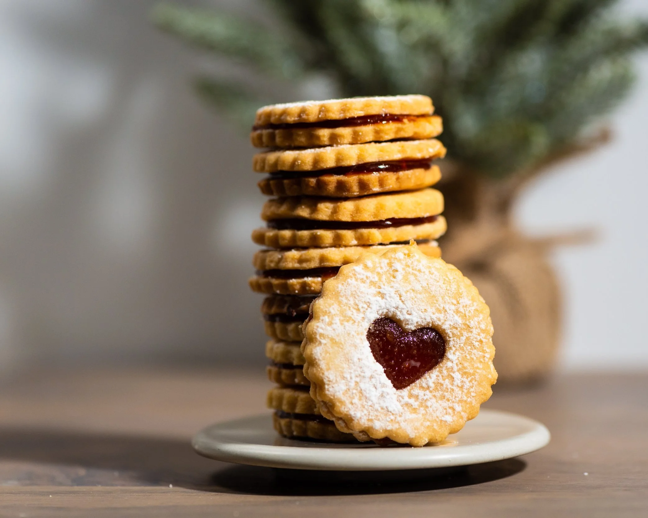 Stack of heart-shaped jam-filled cookies with powdered sugar on a plate.