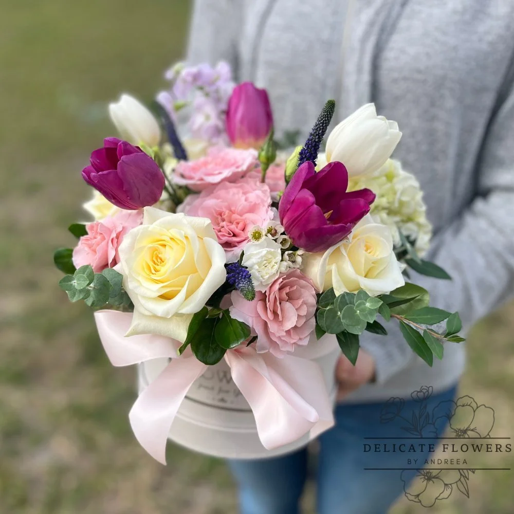 Soft pastel hat box arrangement with ivory roses, pink carnations, purple tulips, hydrangea, and eucalyptus