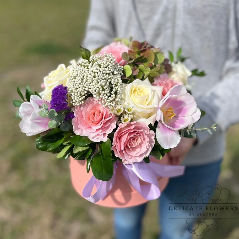 Pink hat box arrangement with blush and ivory roses, pink tulips, white waxflower, and lush greenery