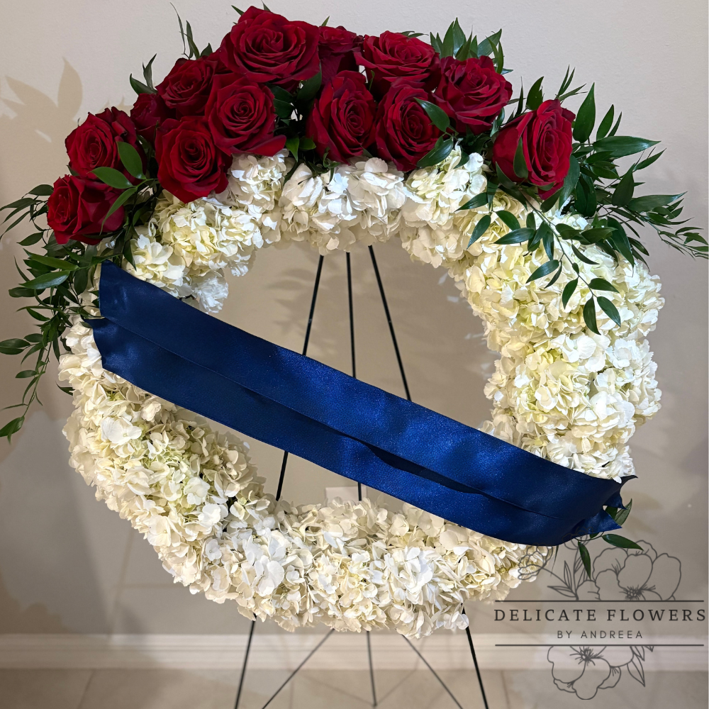 Standing funeral wreath with white hydrangeas, deep red roses, and a navy satin ribbon on a black easel — handcrafted by Delicate Flowers by Andreea in Wesley Chapel, Florida
