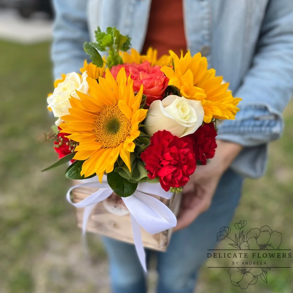 Sunflower arrangement with ivory and coral roses, red carnations, and greenery in a rustic wooden box