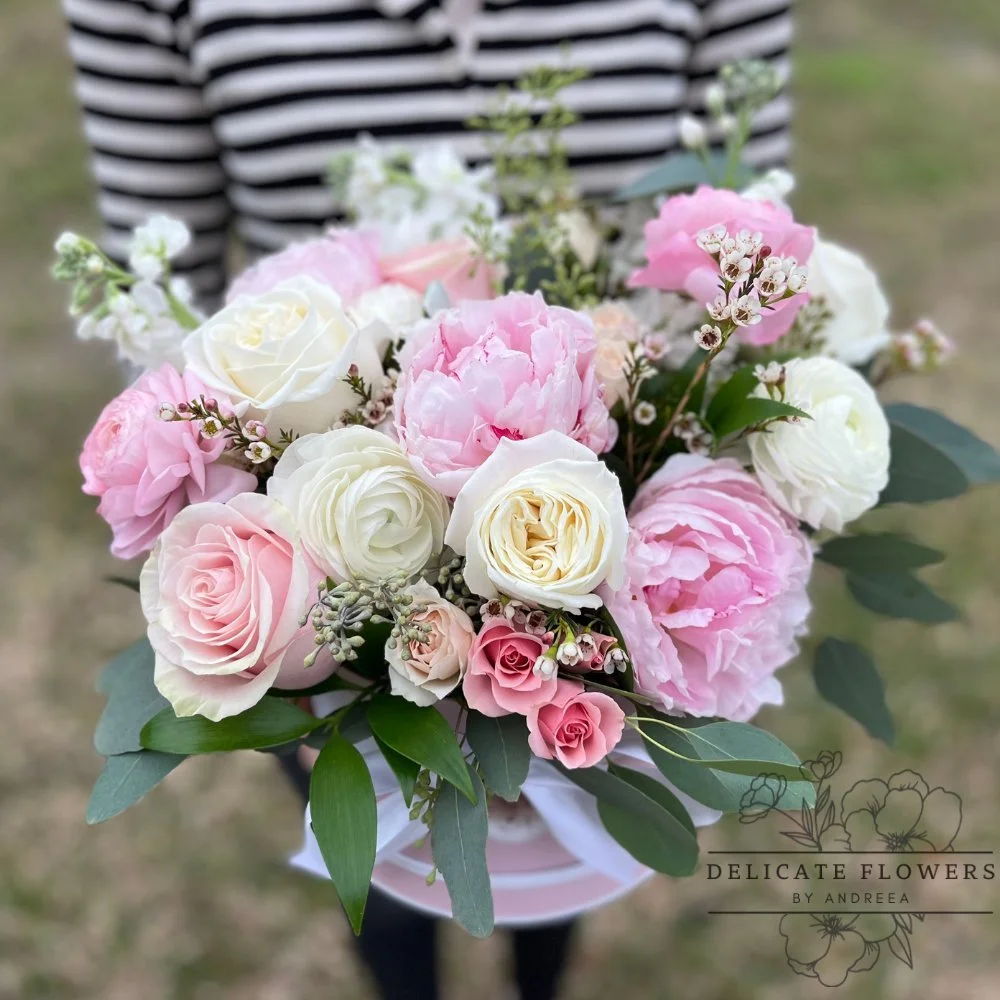 Bouquet of pink and white roses, peonies, and greenery held by a person in a striped shirt.