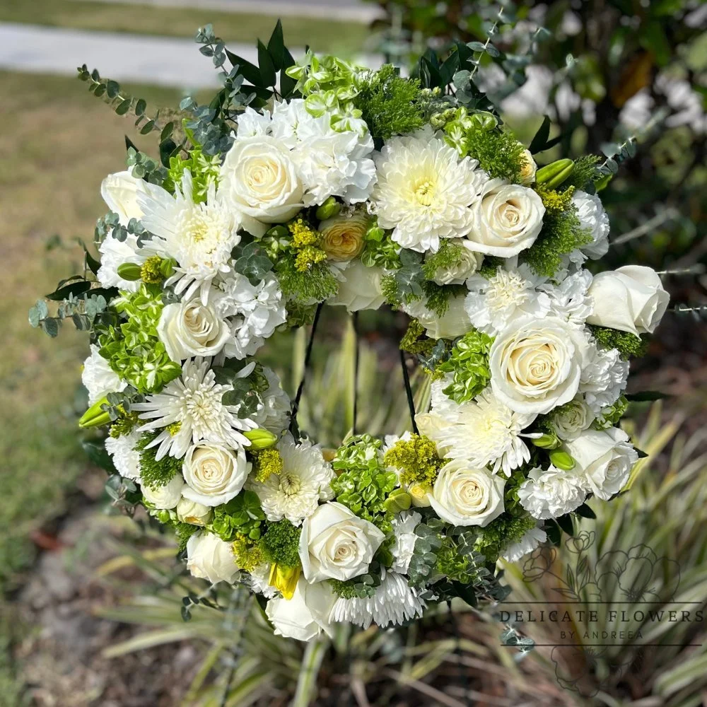 White and green sympathy wreath with ivory roses, mums, hydrangea, lilies, eucalyptus, and seasonal greenery