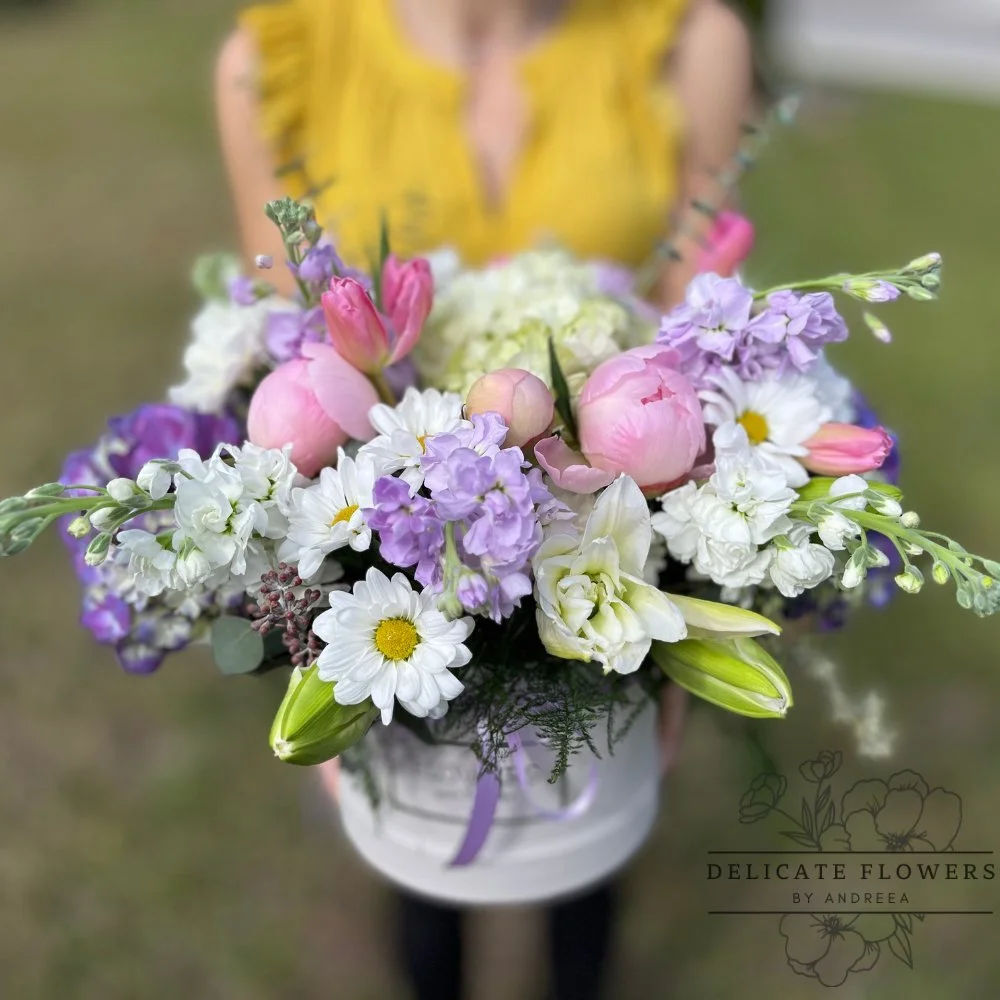 Blushing Spring hatbox flower arrangement with peonies, tulips, daisies, hydrangea, lilies, and lilac stock. Handcrafted same-day in Wesley Chapel, FL. Call Delicate Flowers by Andreea.