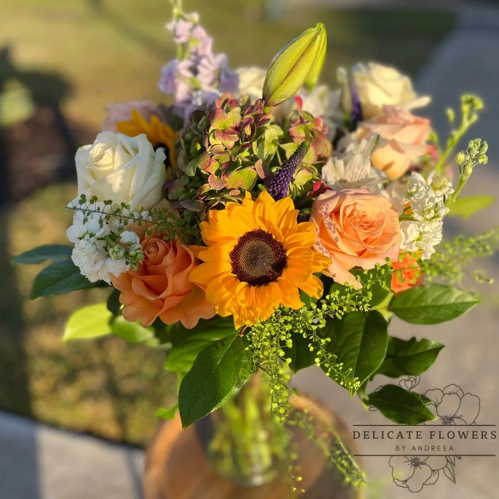 Sunflower bouquet with peach and ivory roses, hydrangea, lilies, and seasonal blooms in a glass vase