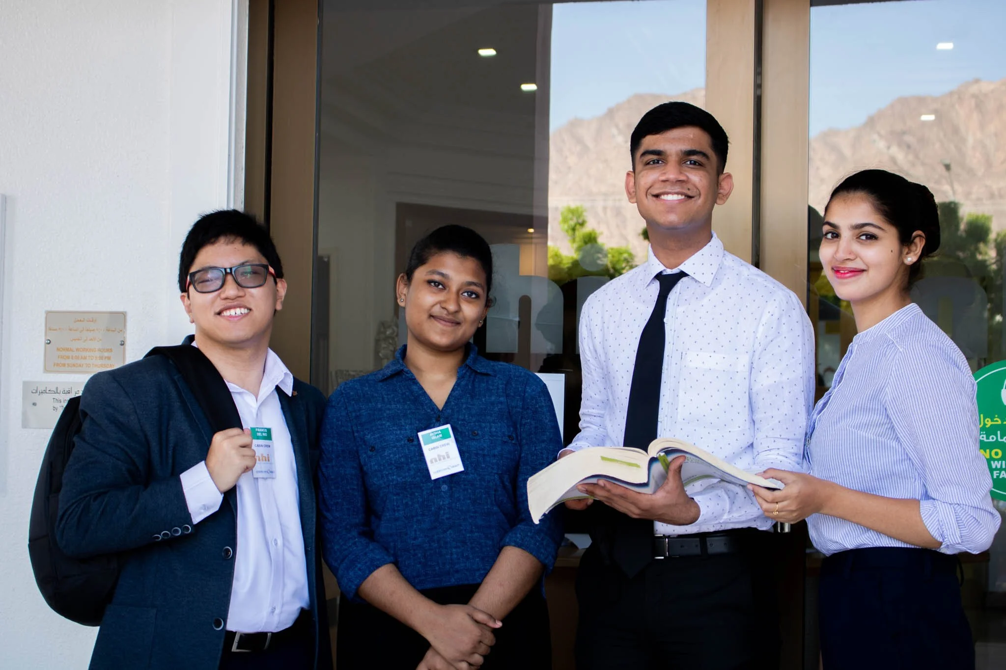 A group of NHI students standing outside the entrance holding a book