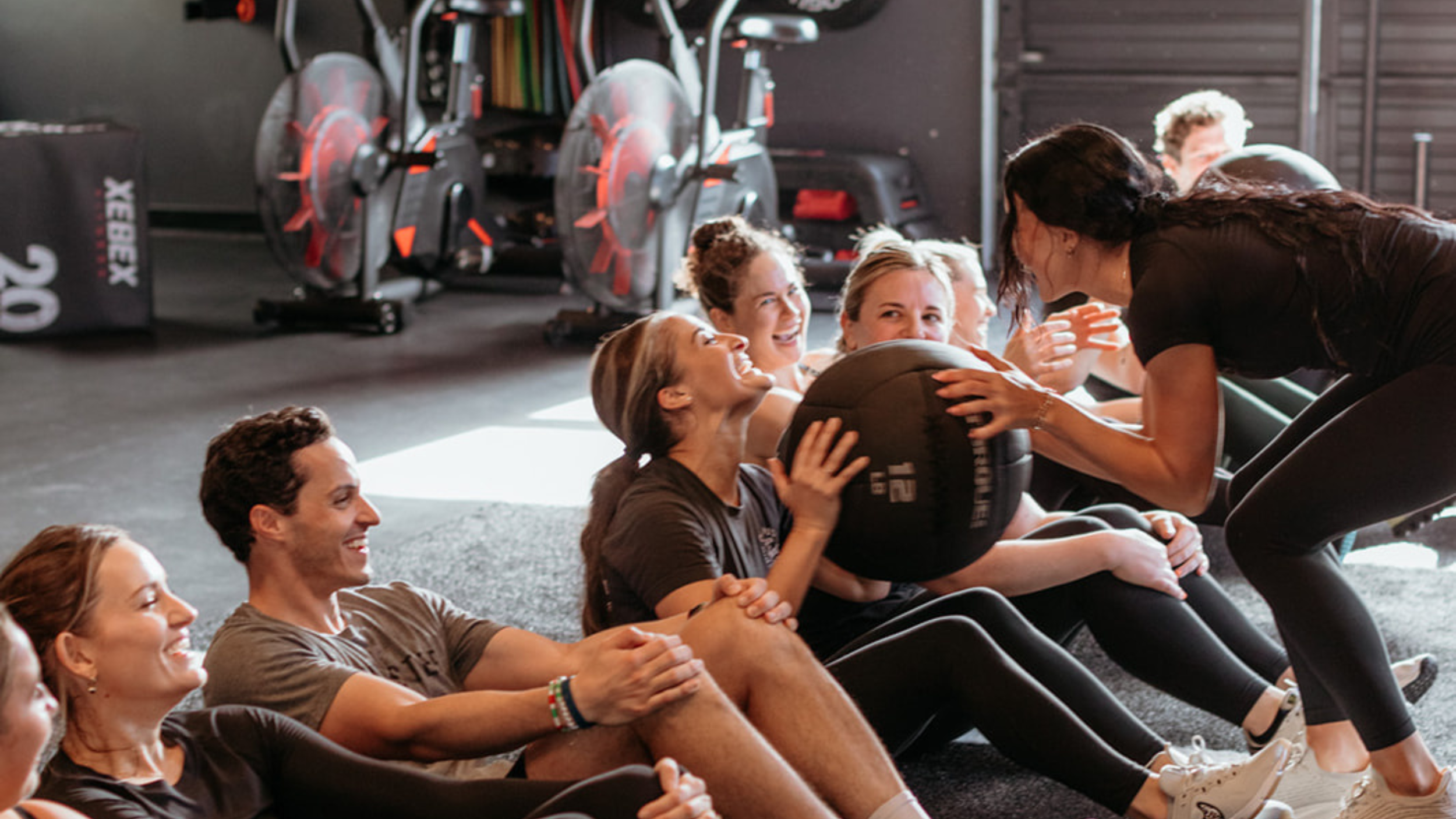 Personal trainer handing a weighted ball to a member smiling in the gym