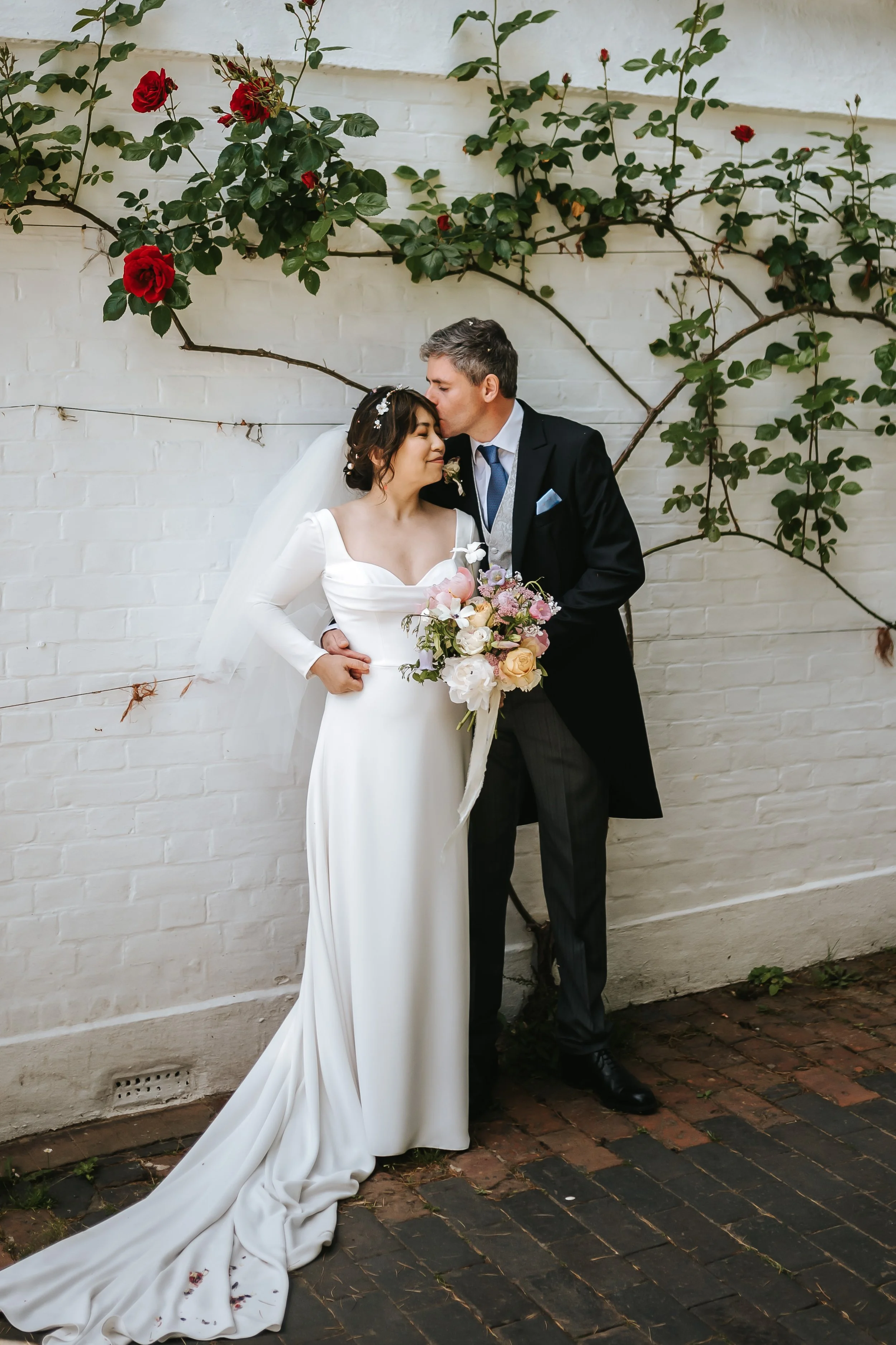 wadhurst-wedding-couple-kiss-climbing-roses-white-wall-portrait.jpg