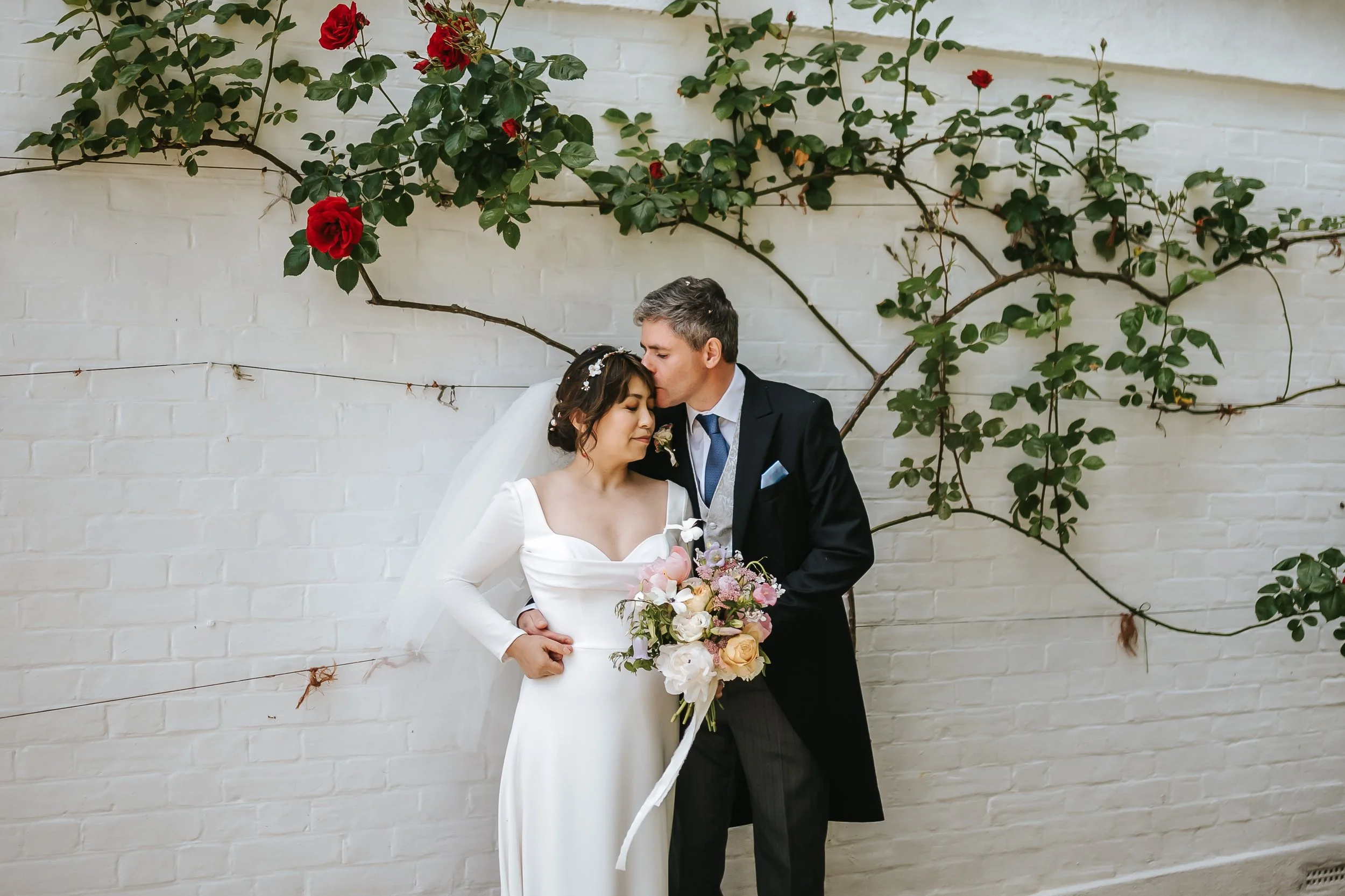 wadhurst-wedding-couple-forehead-kiss-red-roses-wall.jpg